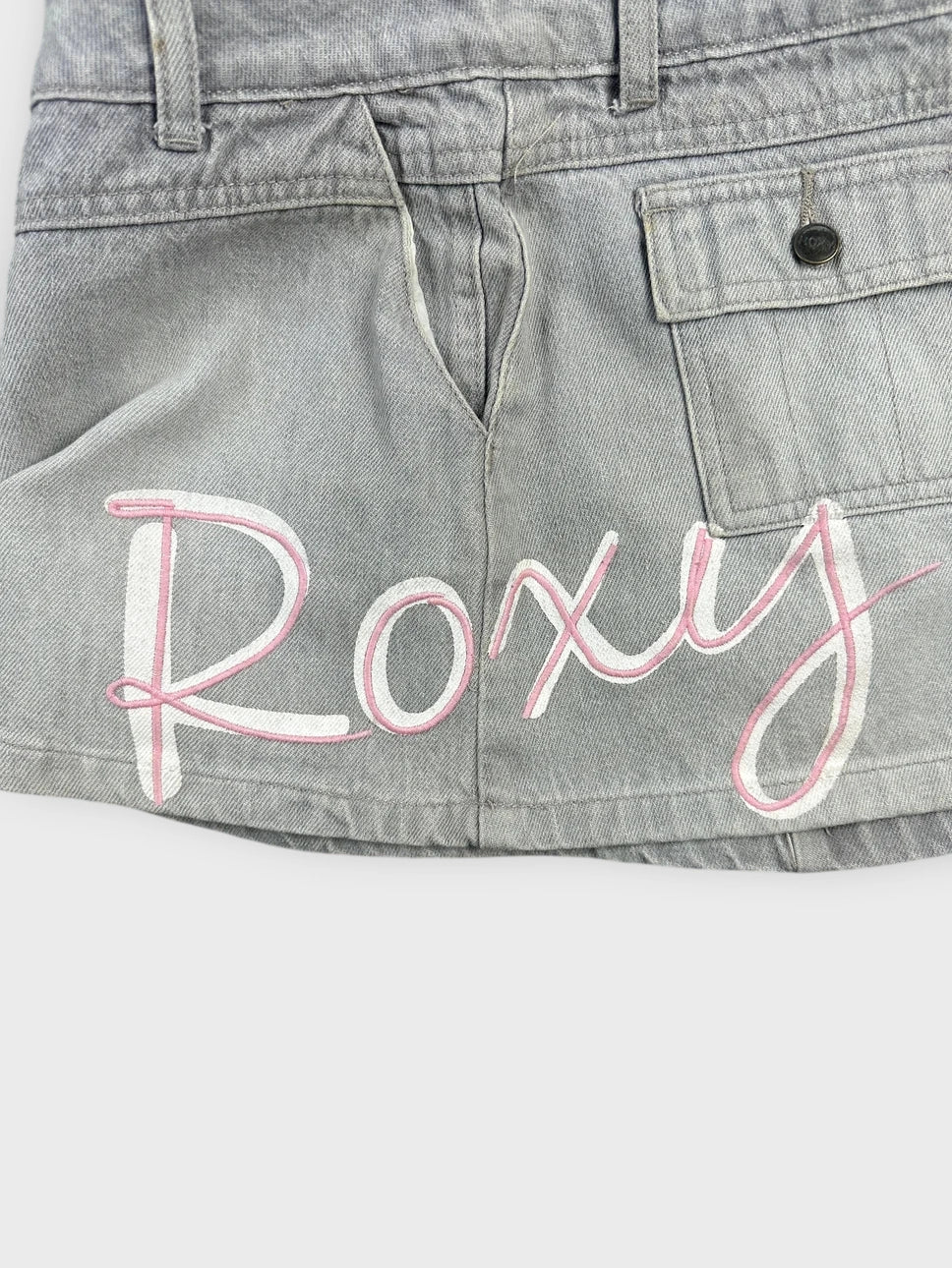 Detail view of grey denim mini skirt with pink embroidered detail.
