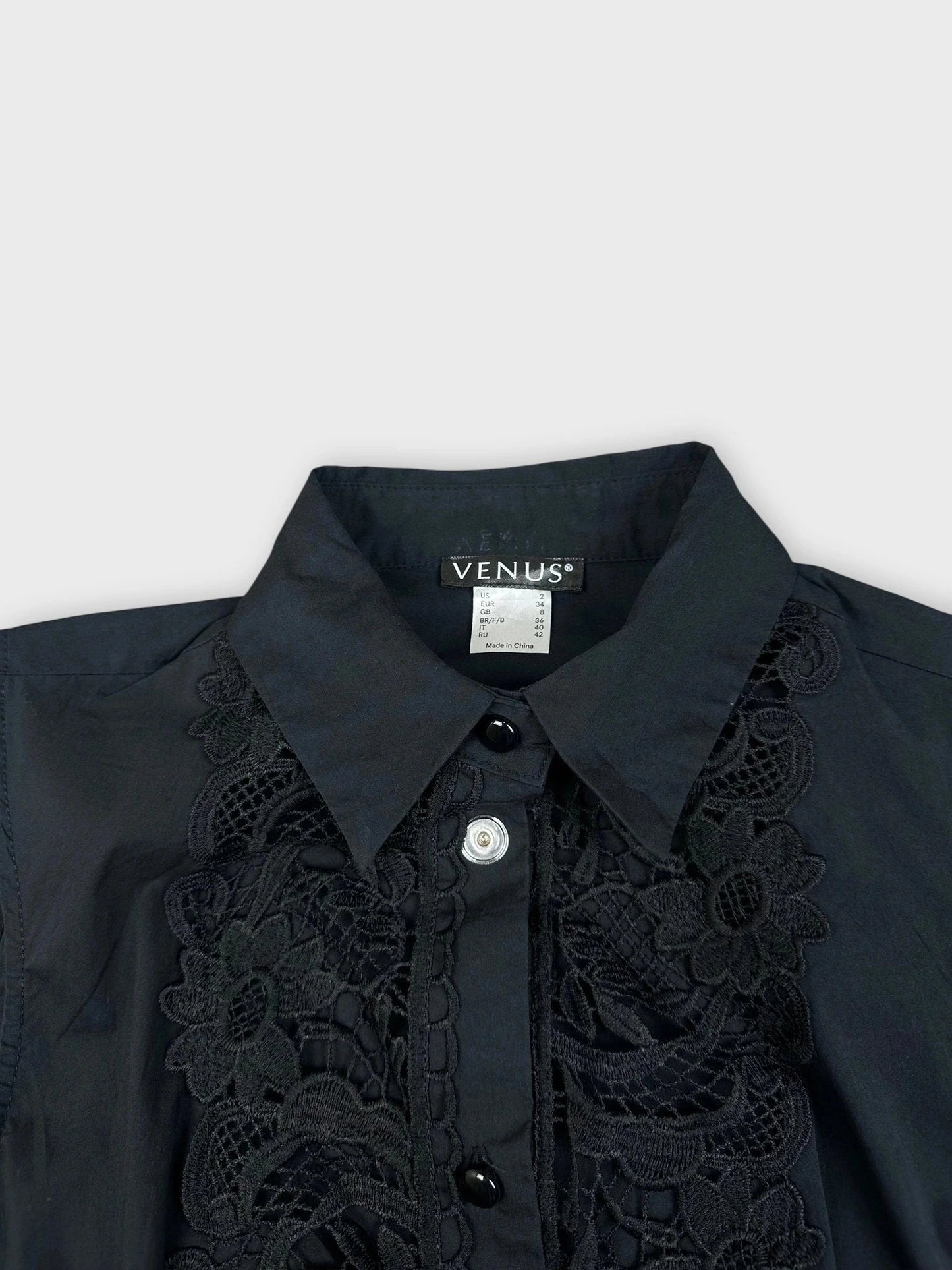 Detail view of black blouse featuring lace detailing and button-up collar.