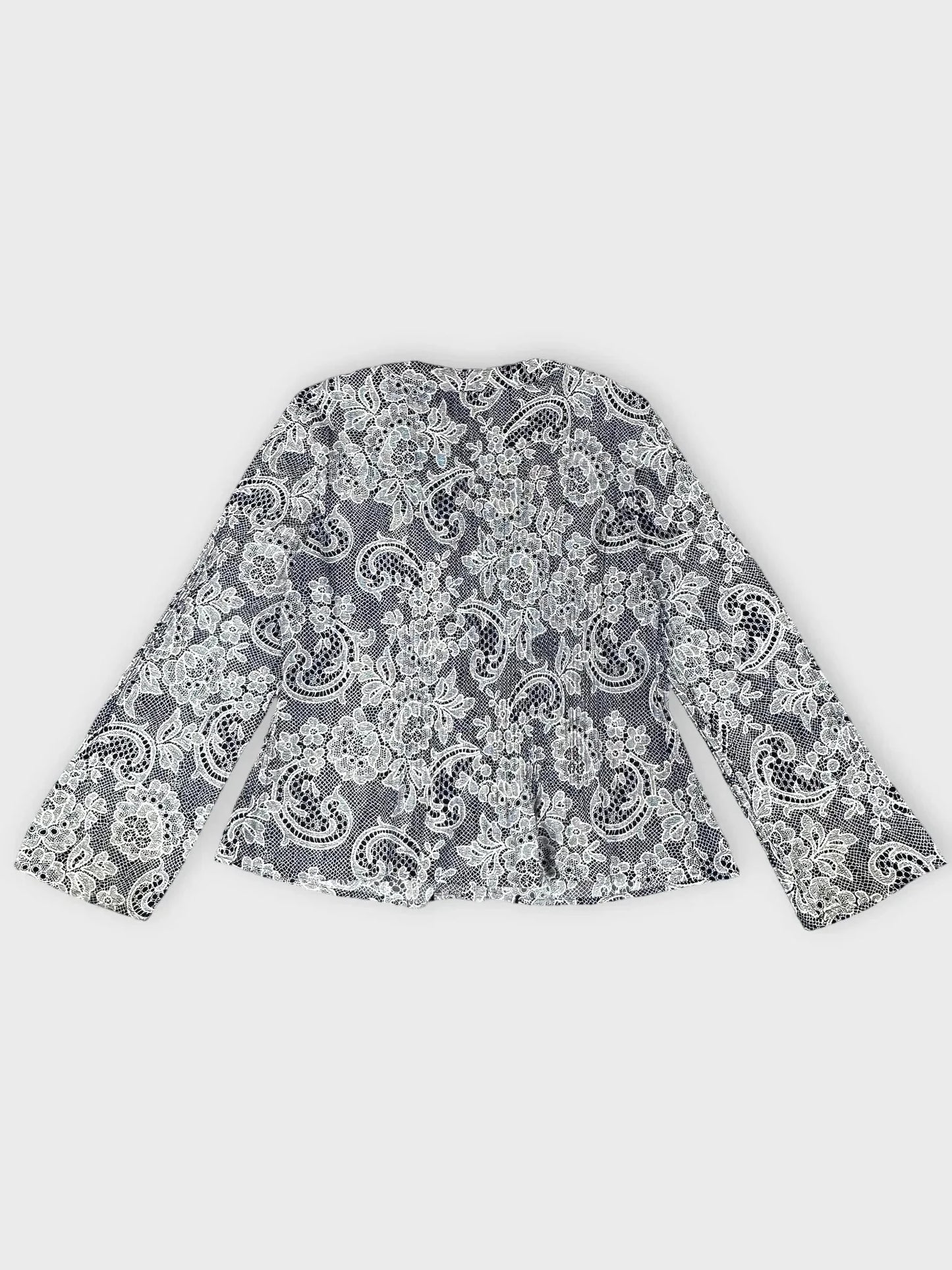 Back view of a lace-print button-up blouse in black and white with ruffle trim.
