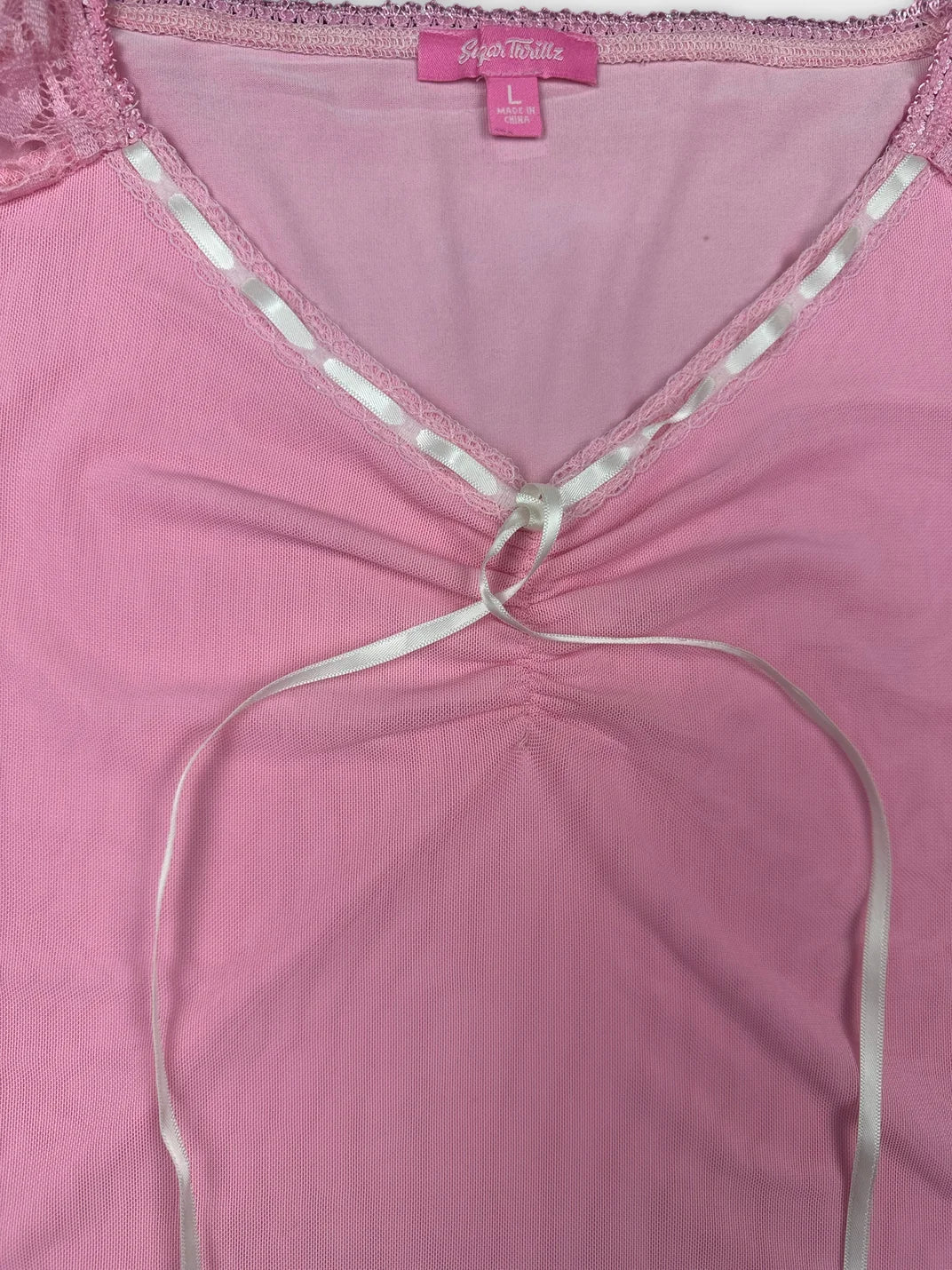 Detail view of a pink crop top featuring lace trim and a tie.