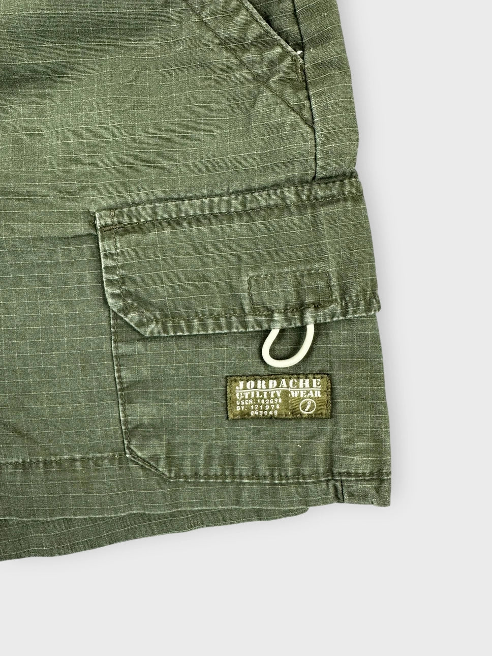 Detail view of olive cargo mini shorts featuring a side pocket and branded tag.