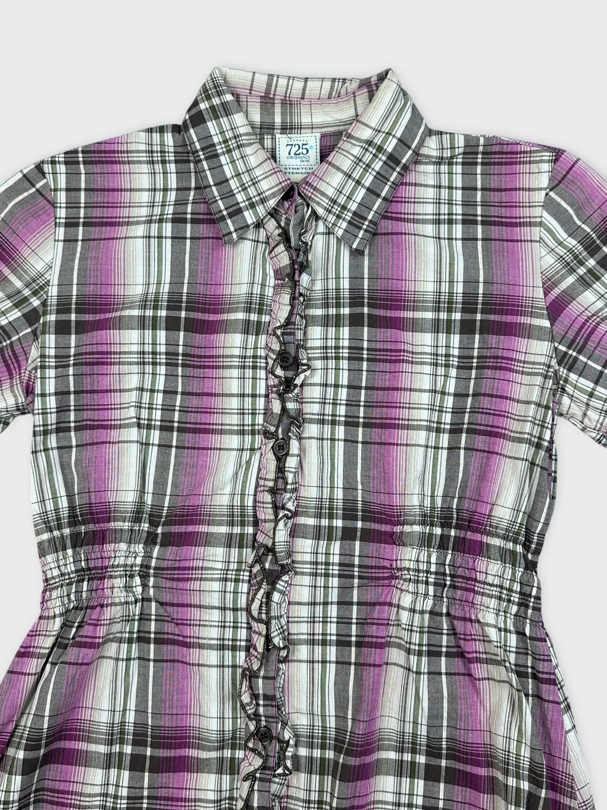 Detail view of a purple plaid button-up peplum shirt with ruffled trim.