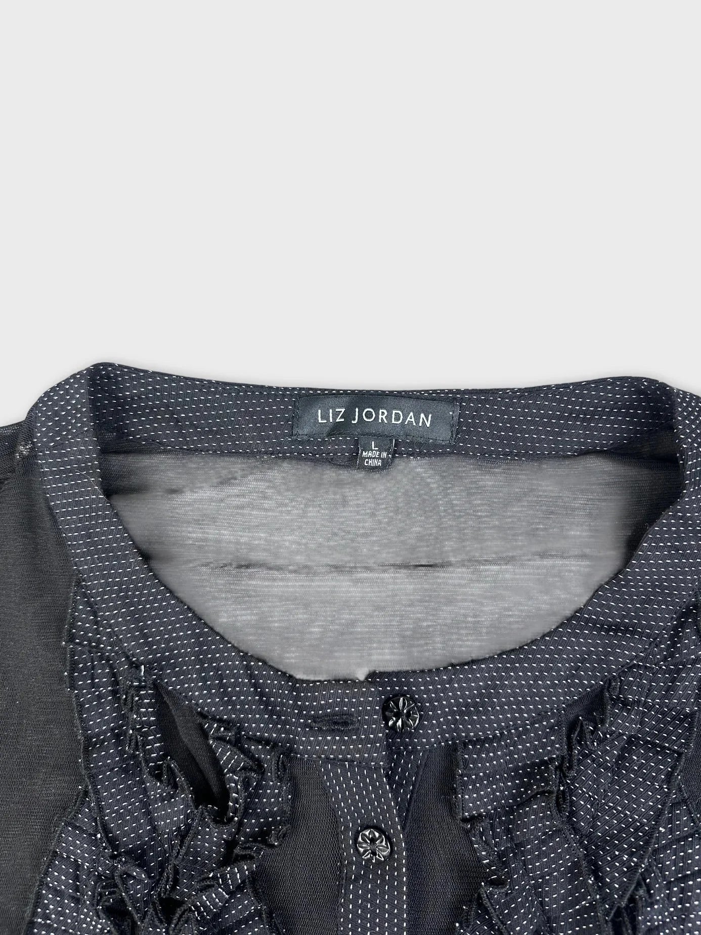 Detail view of sheer black button-up top with ruffle detail.