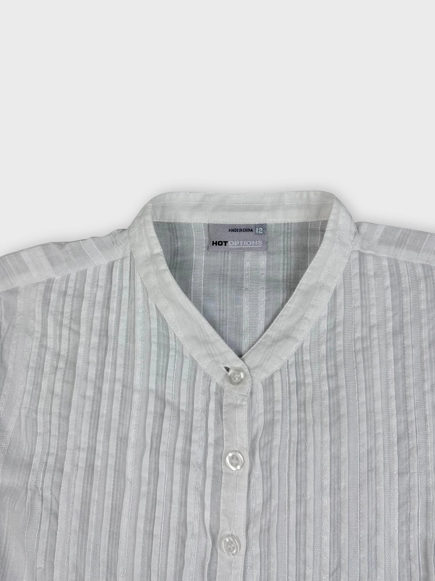 Detail view of a sheer white blouse featuring pintucks and a Mandarin collar.