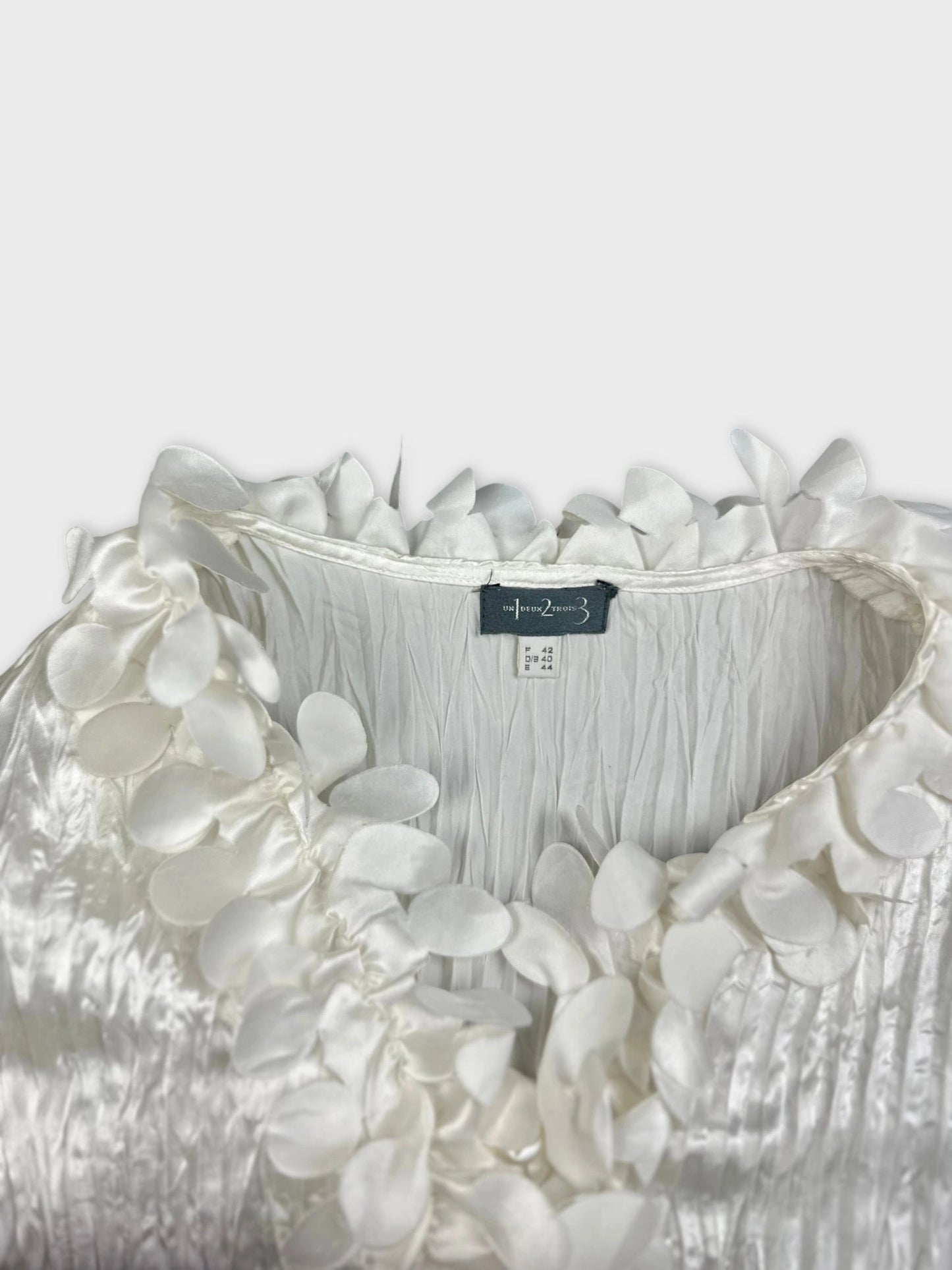 Detail view of a shiny white blouse with floral trim.