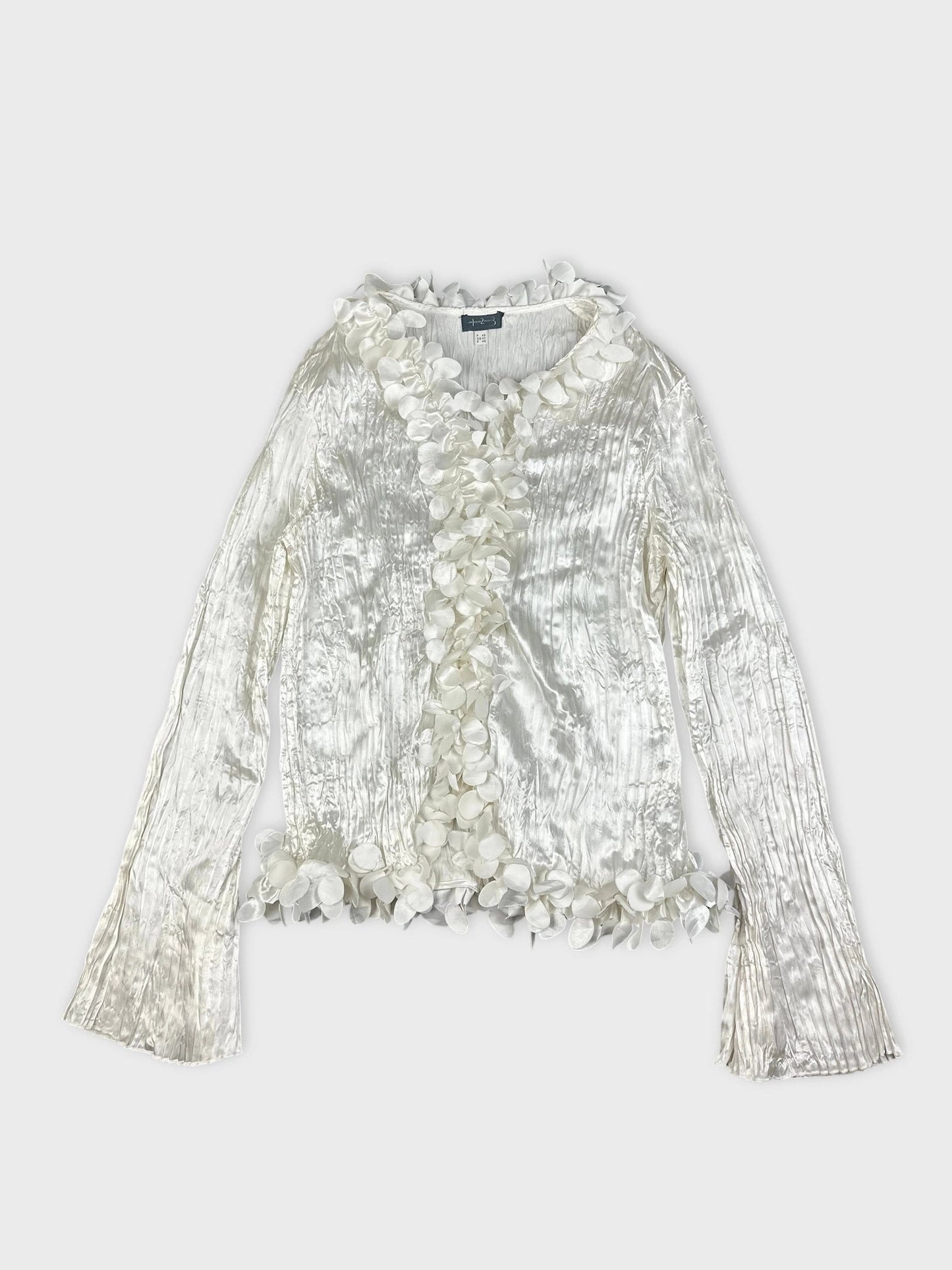 Detail view of shiny long sleeve white blouse with floral trim.