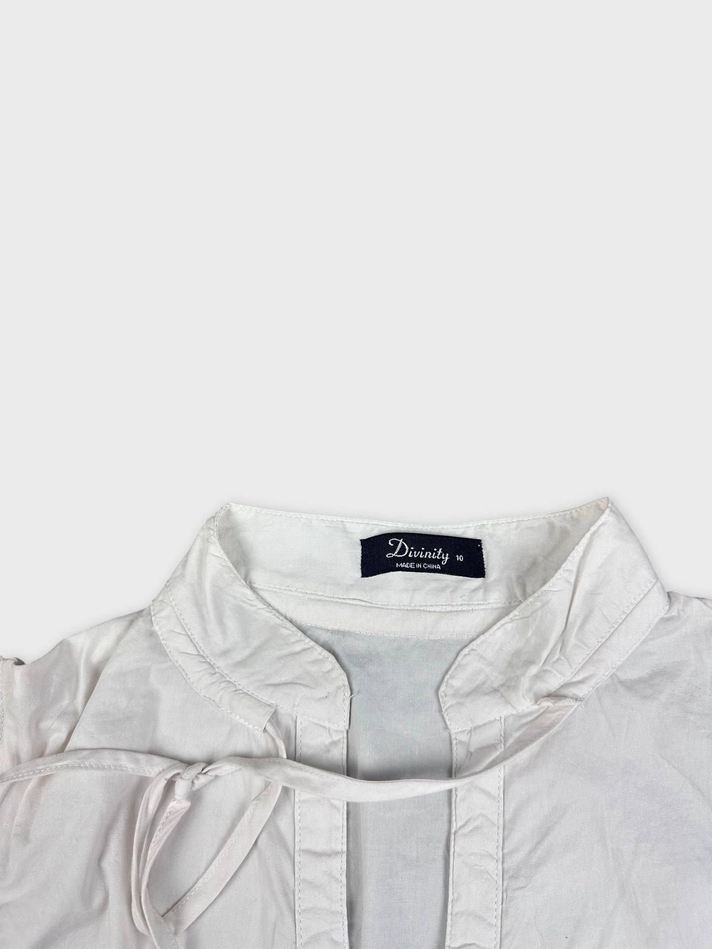 Detail view of short-sleeve white blouse featuring a tie neckline.