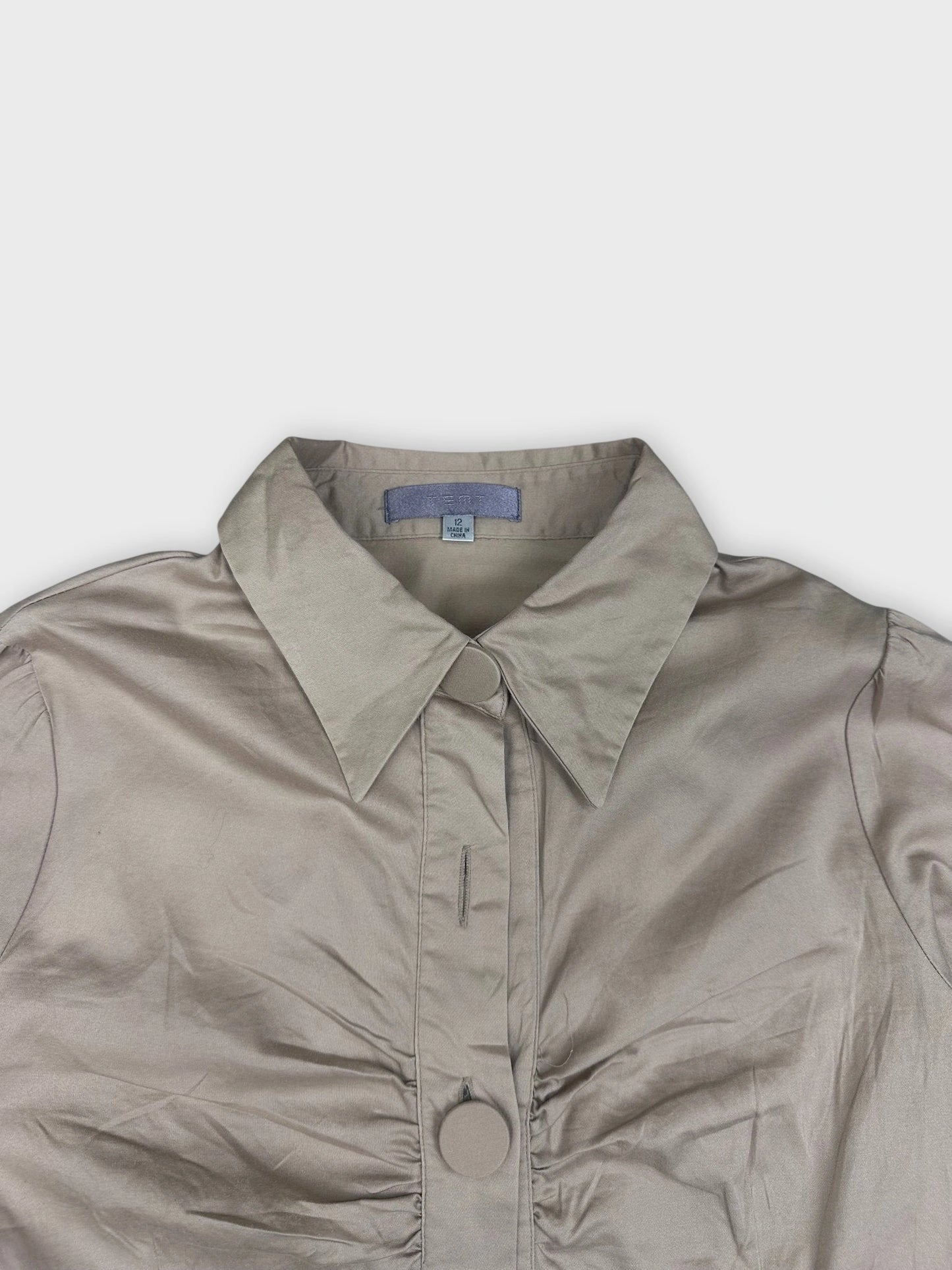 Detail view of beige button-up blouse with ruched bust and large buttons.