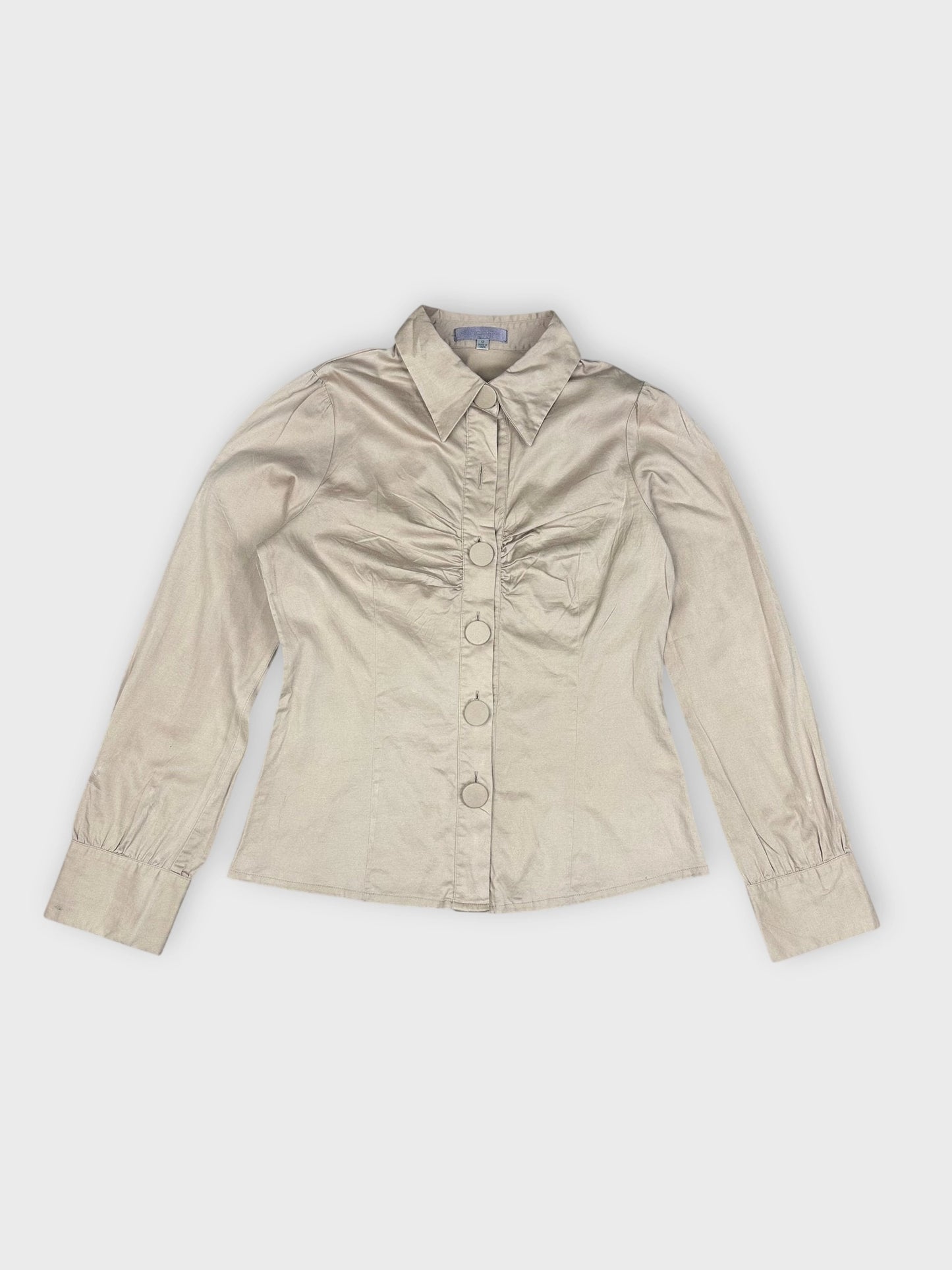 Detail view of beige blouse featuring button-up front and ruched bust.