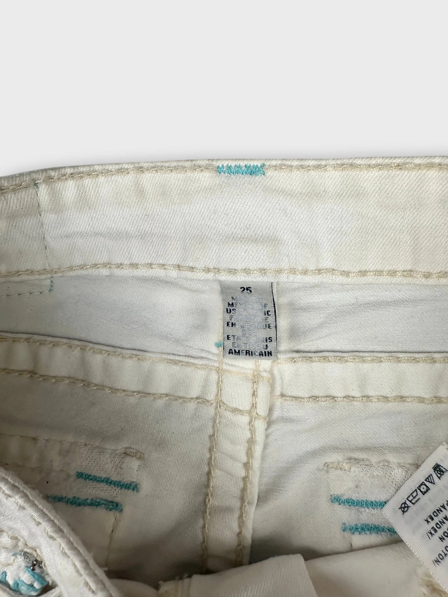 Detail view of white denim shorts with blue stitching accents.