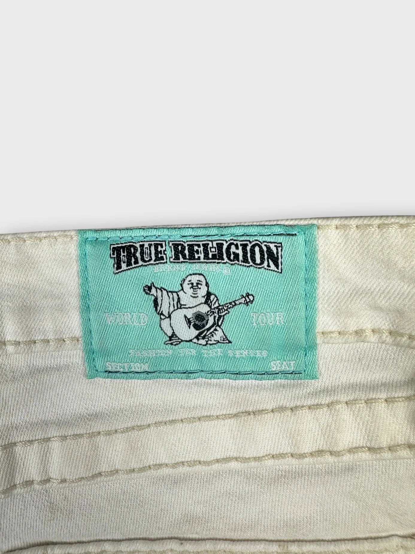 Detail view of white denim shorts featuring a colorful embroidered label.