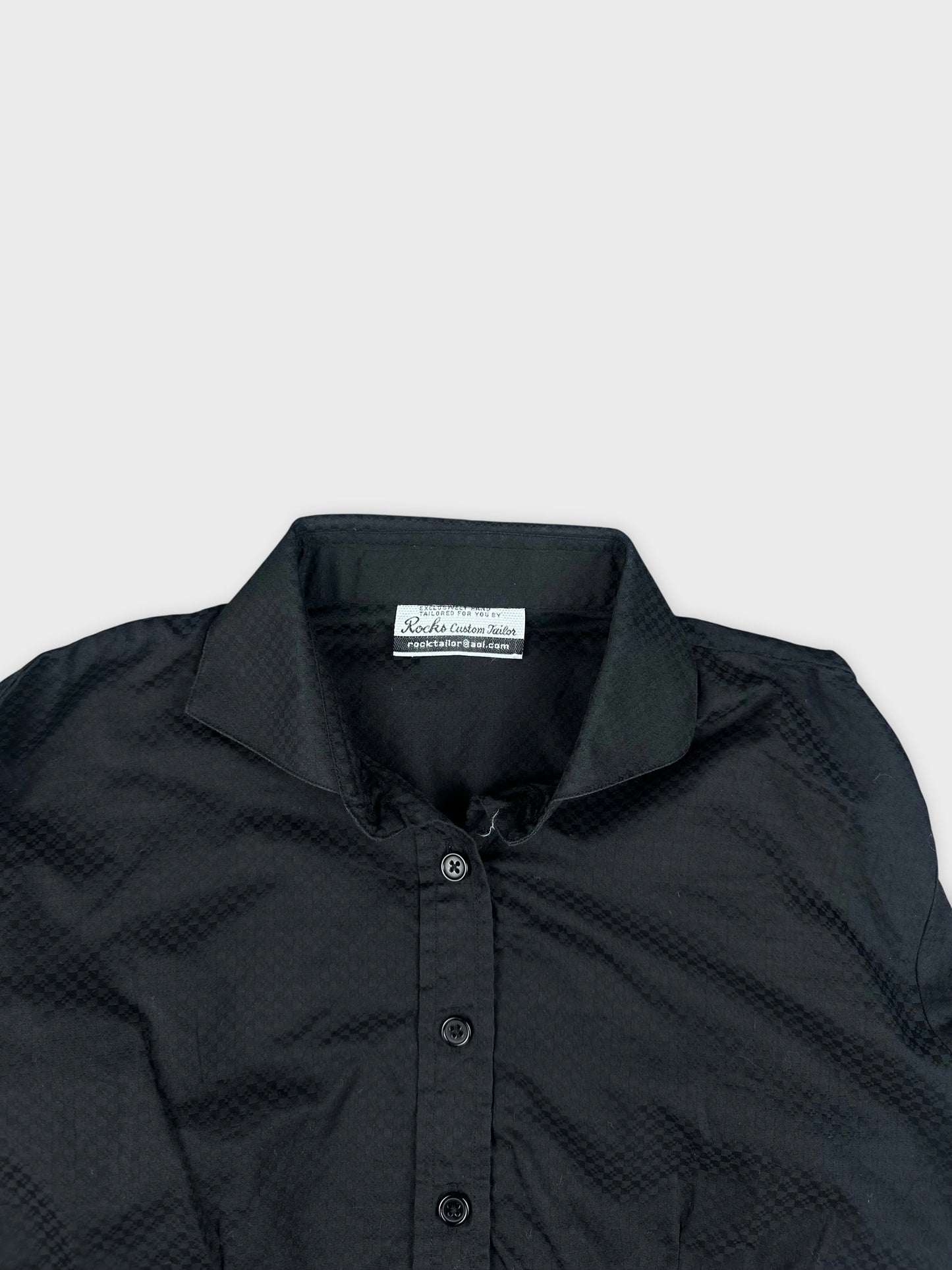 Black shirt detail view featuring textured pattern and button closure.