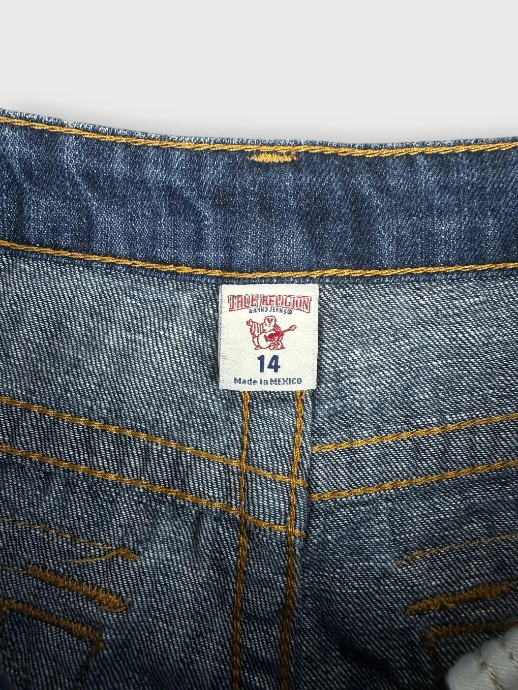 Detail view of blue denim shorts with yellow stitching and brand tag.