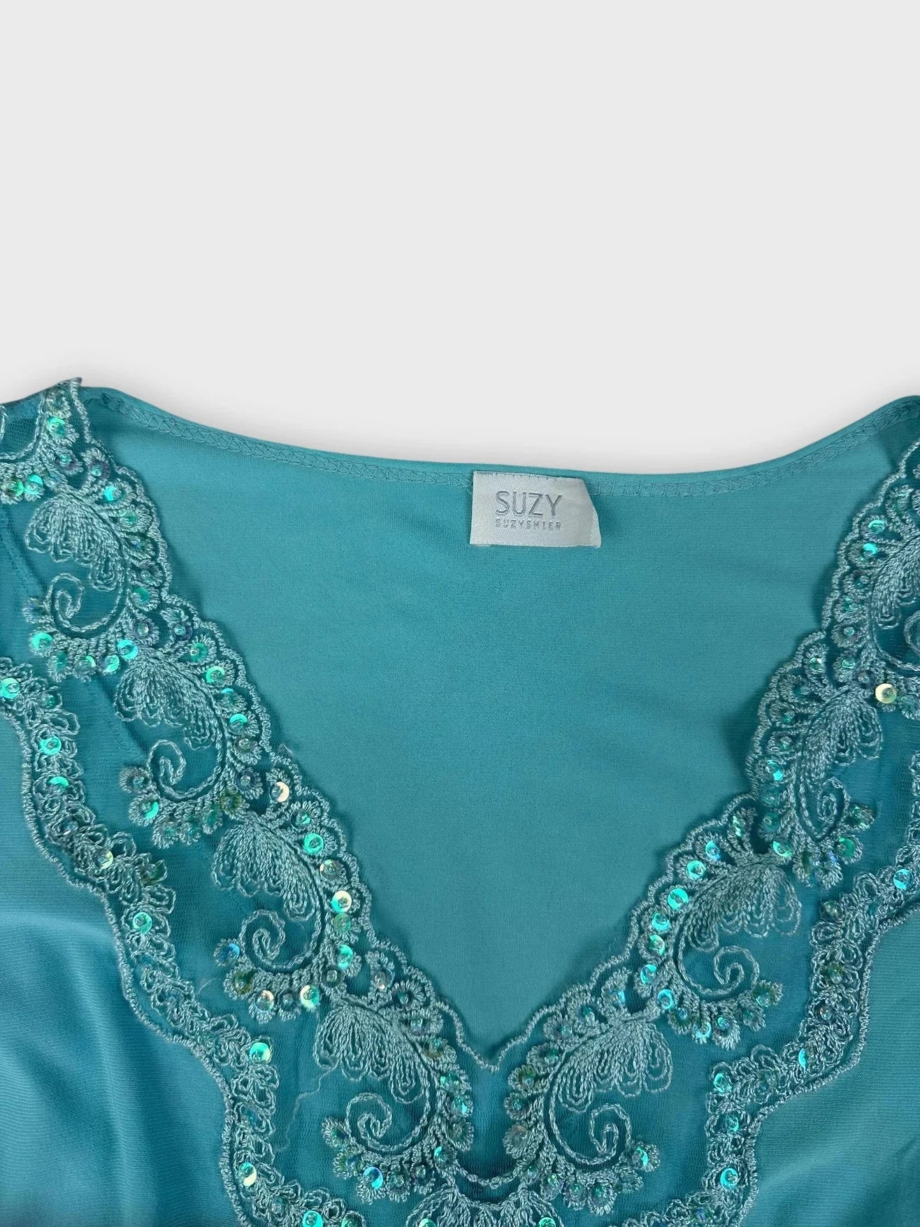 Detail view of turquoise embroidered short sleeve top featuring intricate neckline embellishments.