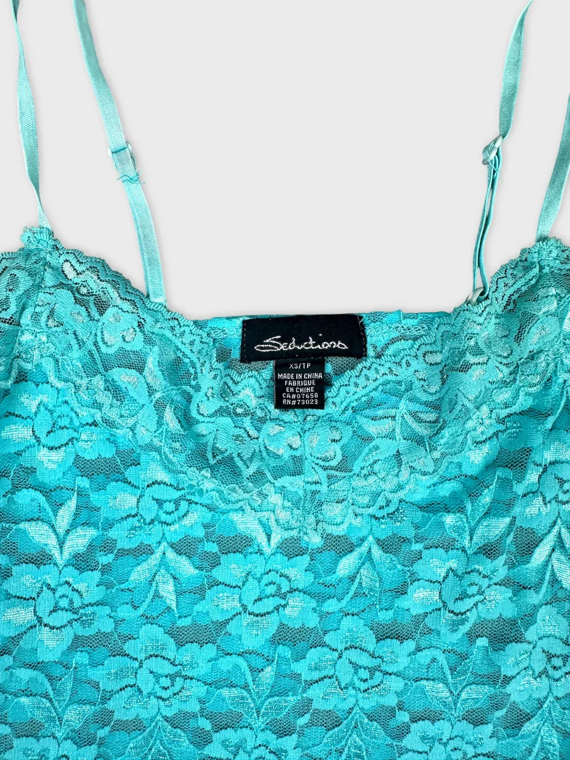 Detail view of turquoise lace top with delicate straps and floral pattern.