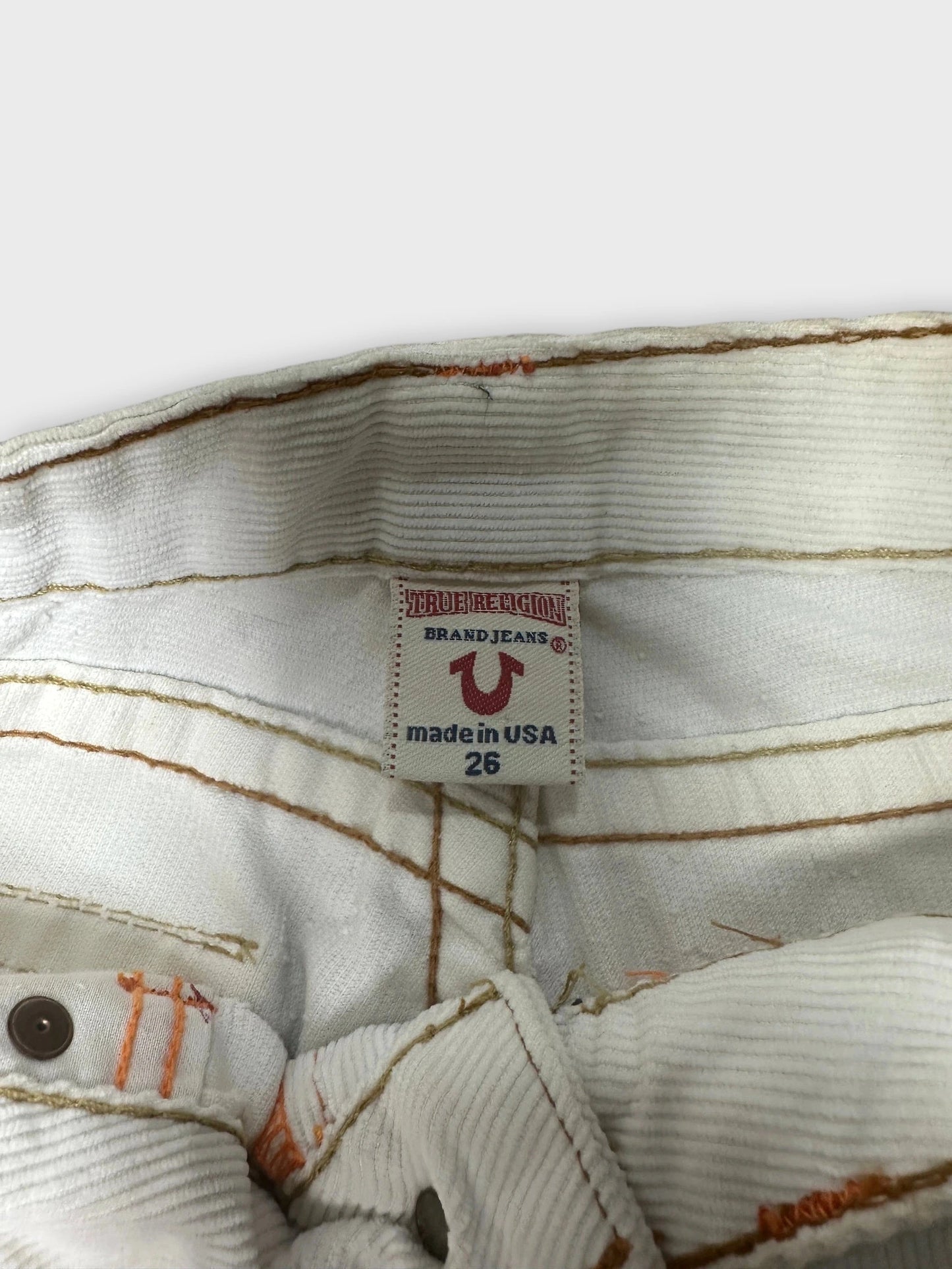 Detail view of white denim shorts with orange stitching and brand label.