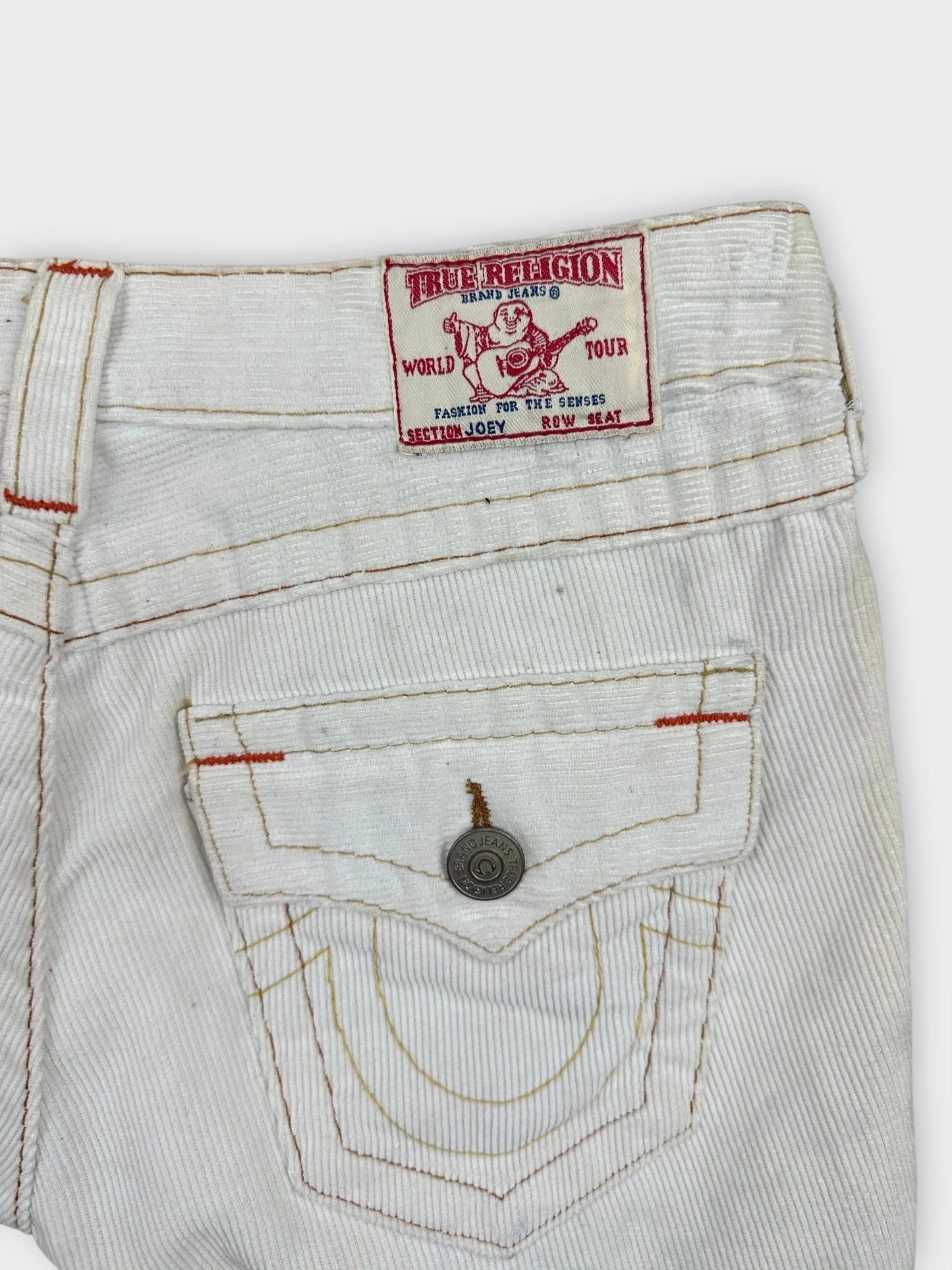 Detail view of white denim shorts featuring red stitching and logo patch.