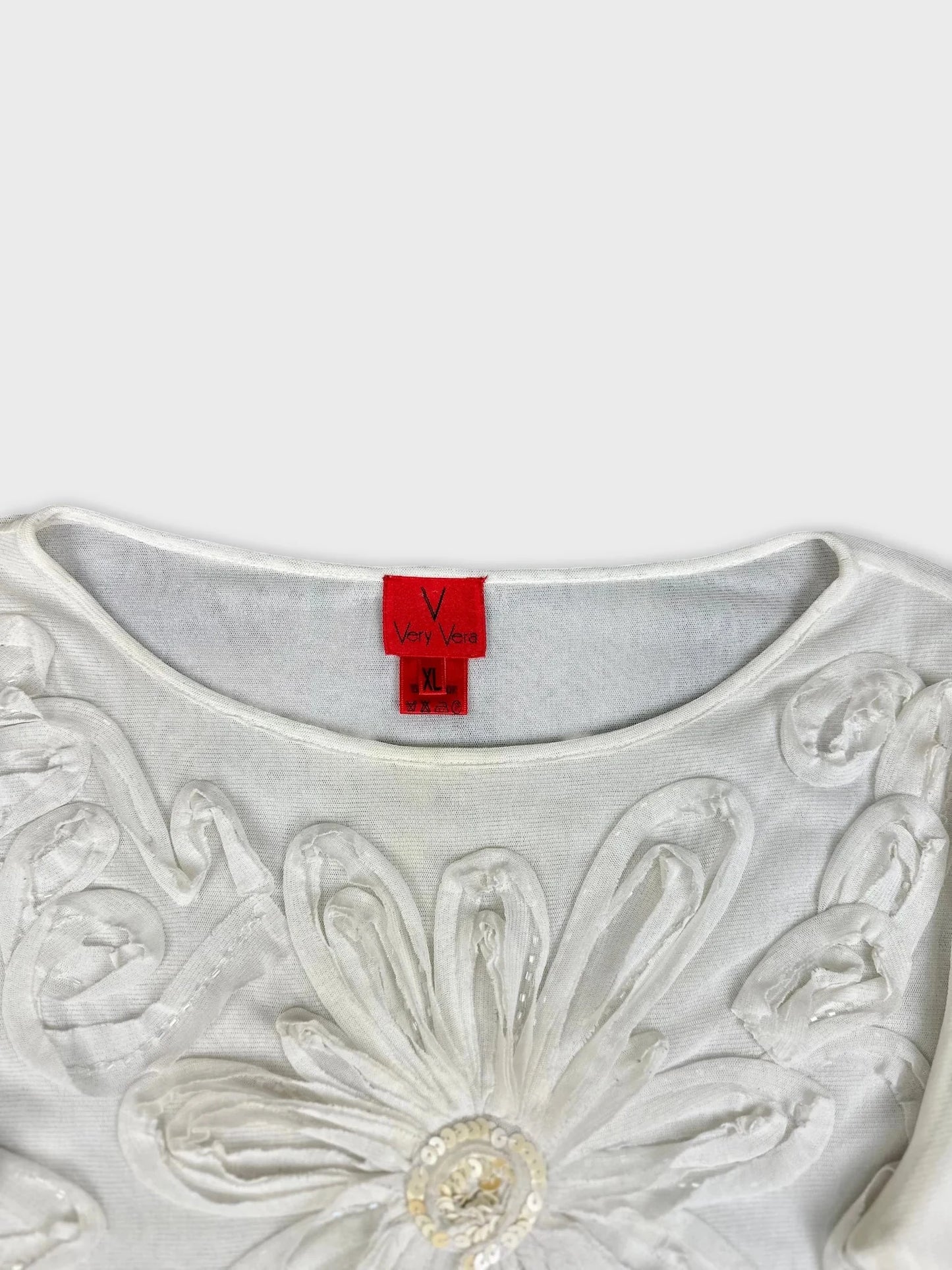 Detail view of white long sleeve top with floral embellishments.