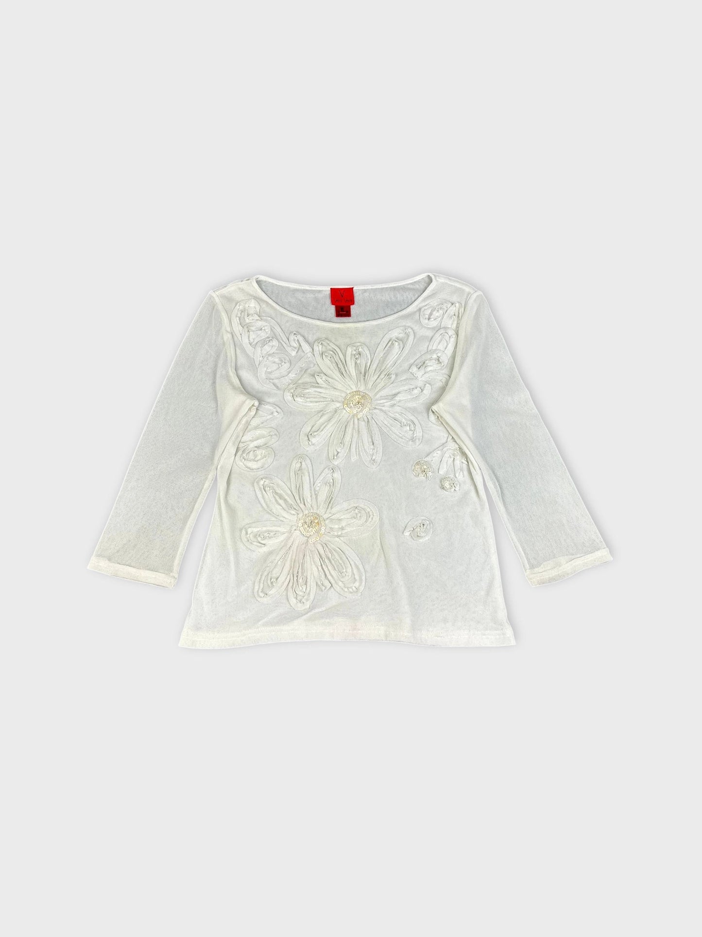 Detail view of white long sleeve top with floral embellishments.