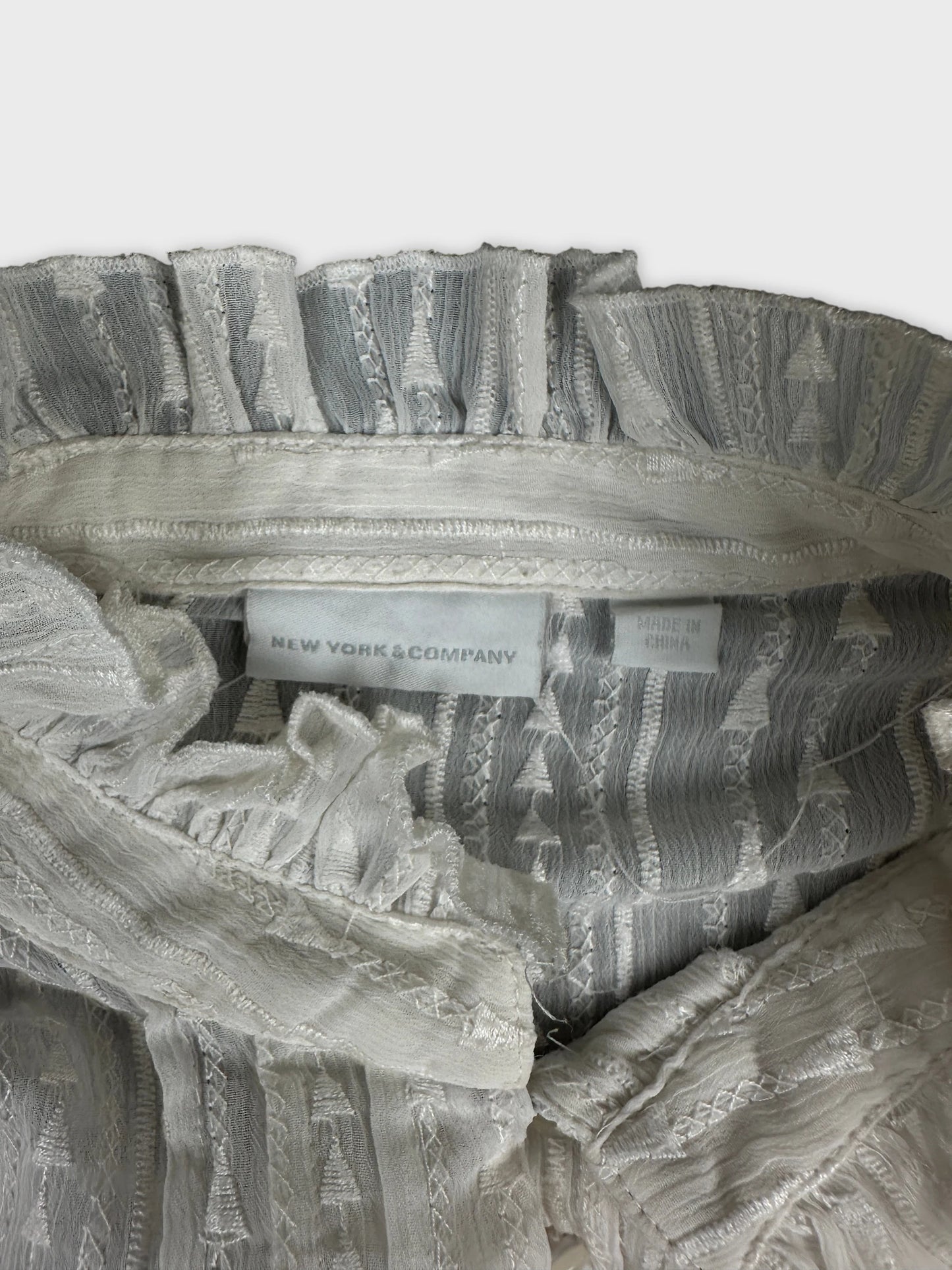 Detail view of a white body shirt with ruffled neckline and textured fabric.