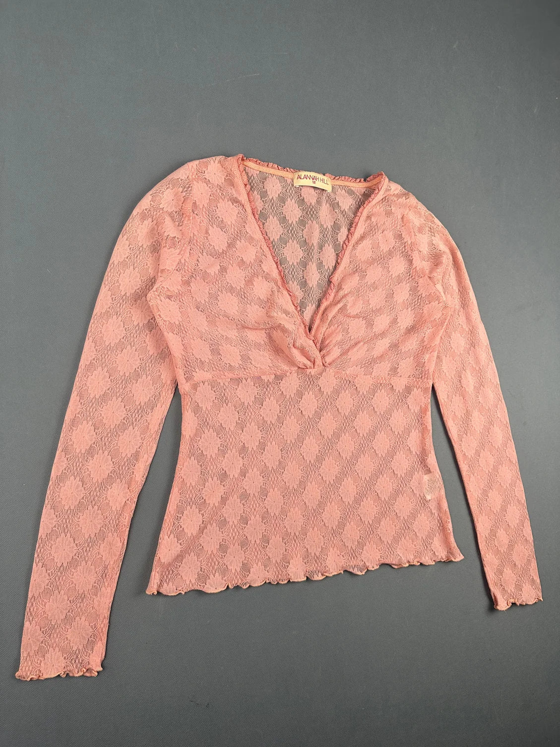 Detail view of women body shirt in light pink with floral pattern and scalloped hem.