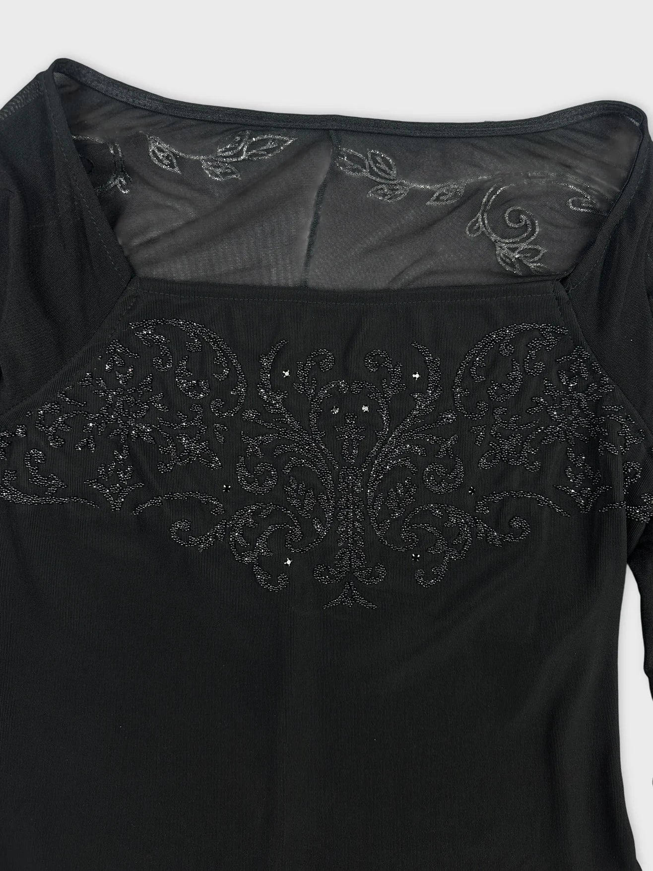 Detail view of a black body shirt featuring intricate black embroidery.