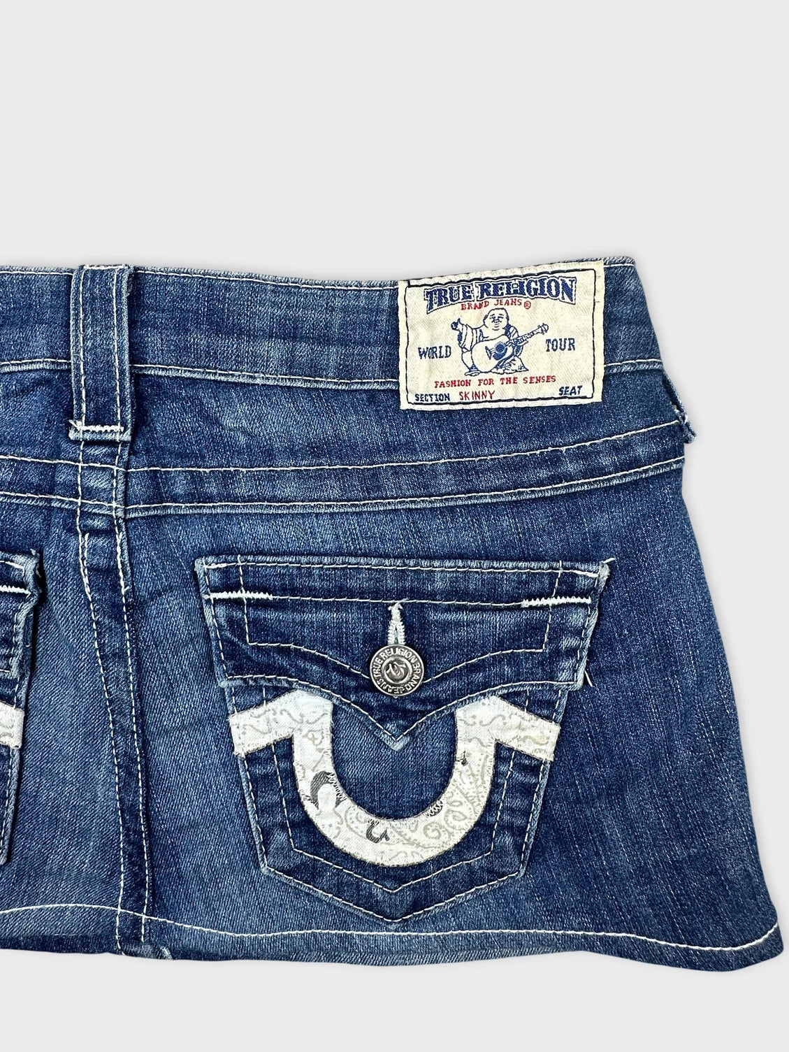 Detail view of a denim skirt in blue with patterned back pockets.
