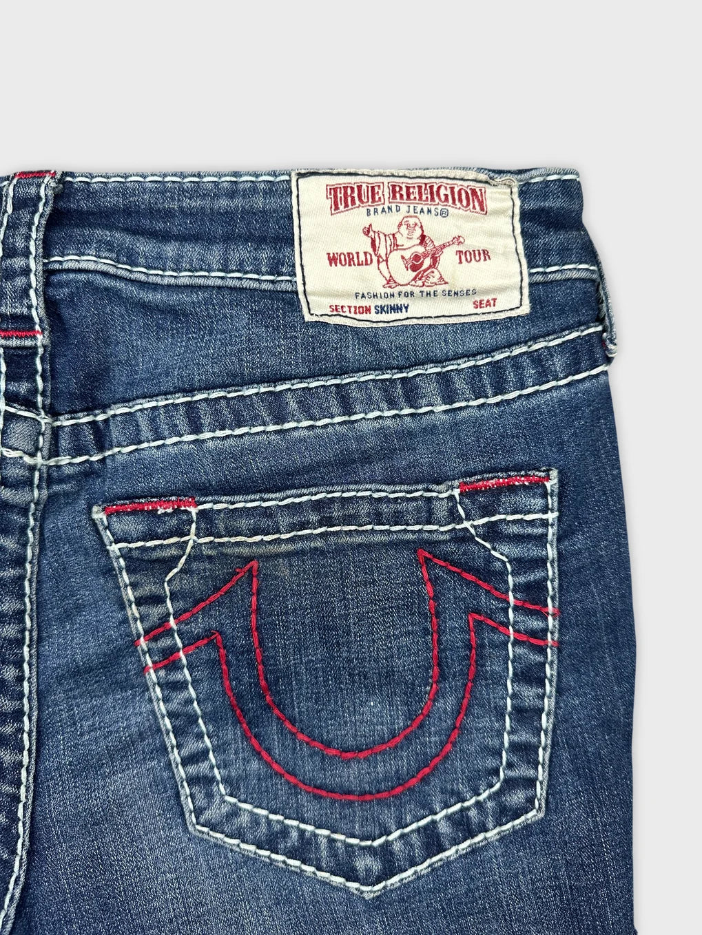 Detail view of denim mini shorts showing red stitching on back pocket.