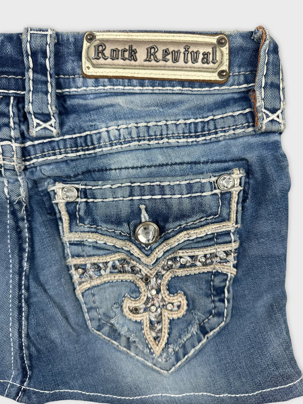 Detail view of denim mini skirt featuring embroidered pocket design in blue.