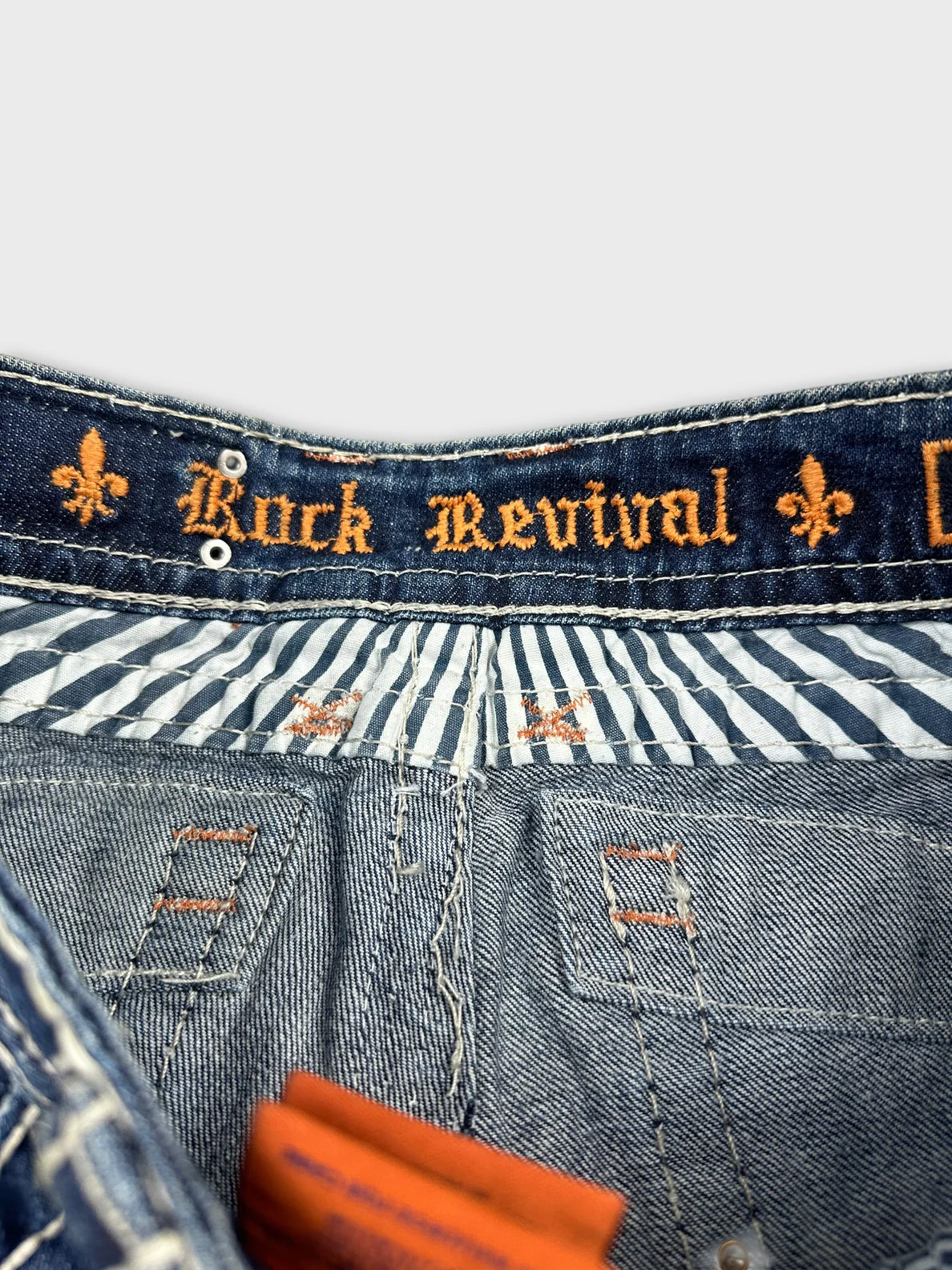Detail view of denim shorts featuring blue color and embroidered 'Rock Revival' logo.
