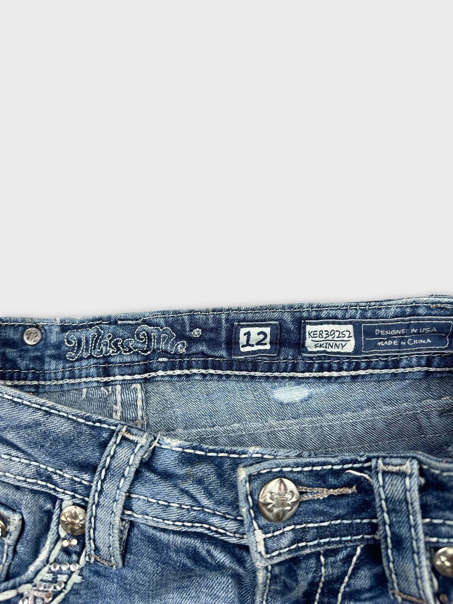 Detail view of blue denim shorts featuring decorative buttons and stitching.