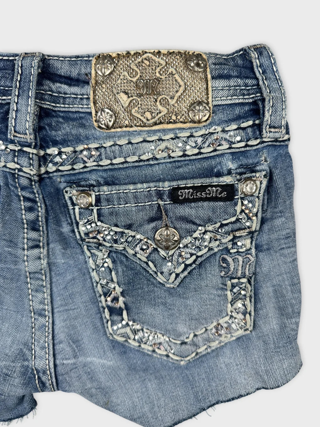 Detail view of denim shorts in blue featuring embellished pockets and stitching.