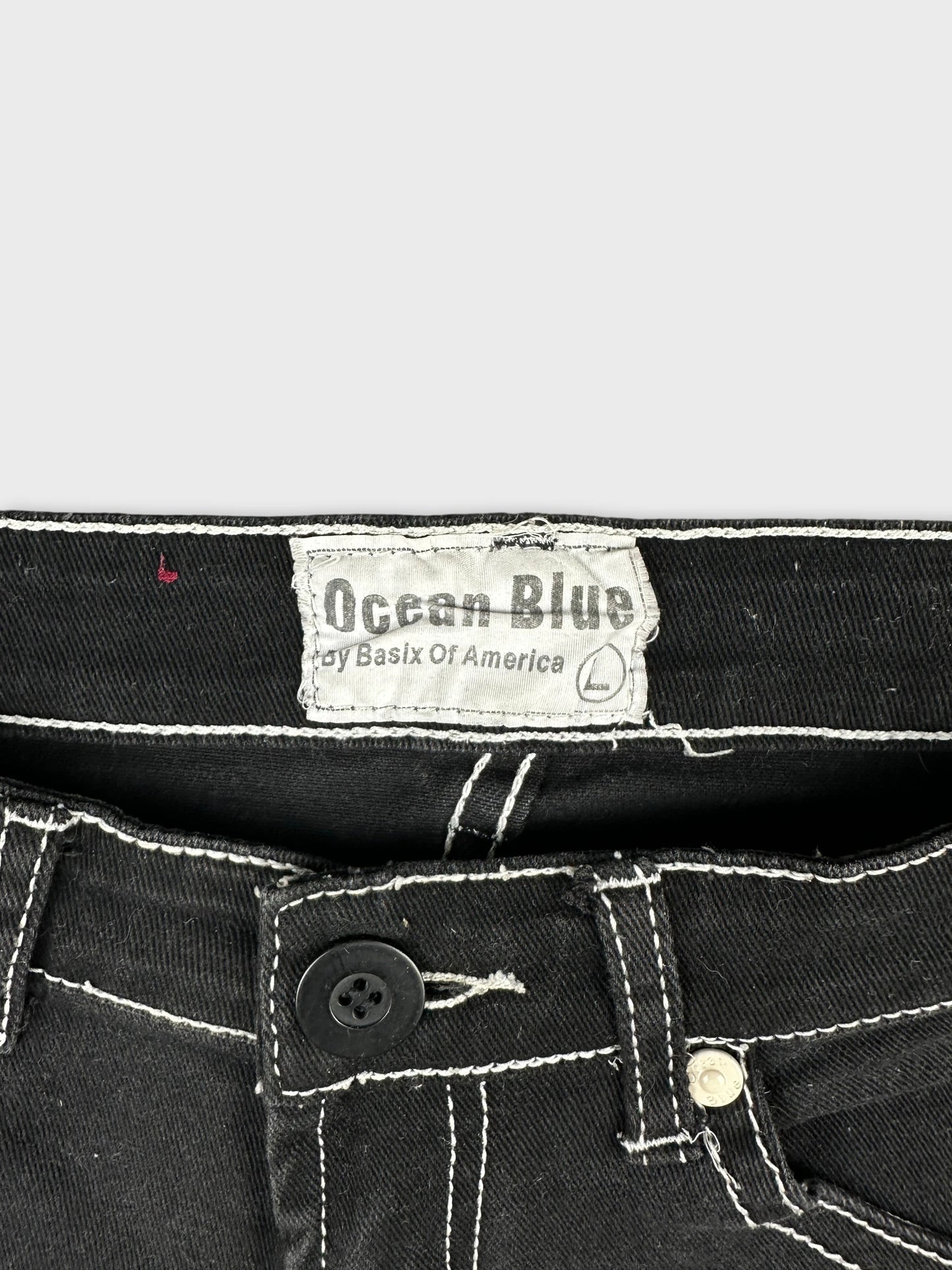 Detail view of black mini shorts featuring white stitching and button closure.