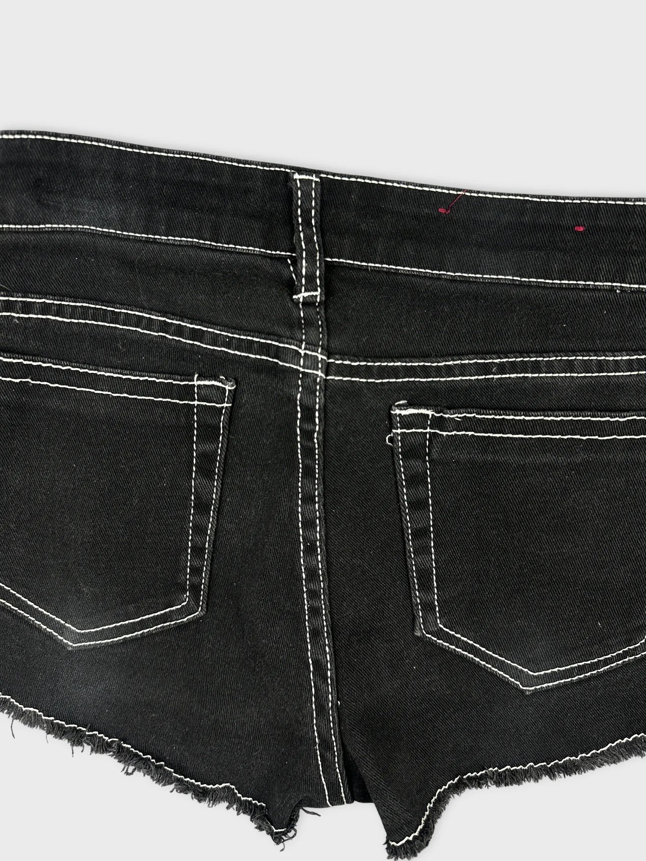 Detail view of black denim mini shorts with frayed hem and contrasting white stitching.