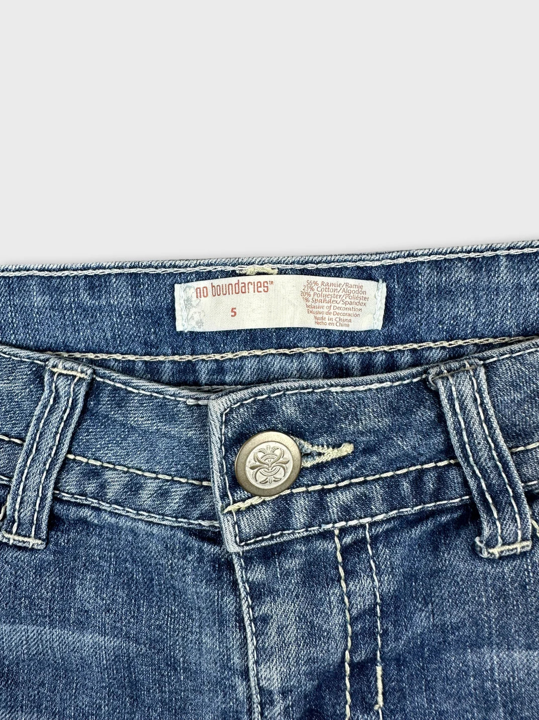 Detail view of blue denim shorts with silver button and contrasting stitching.