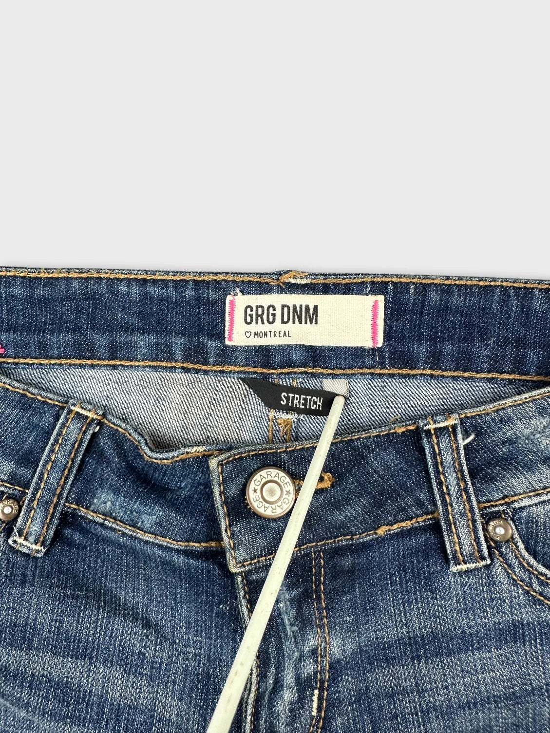 Detail view of blue denim shorts featuring button and stretch label.
