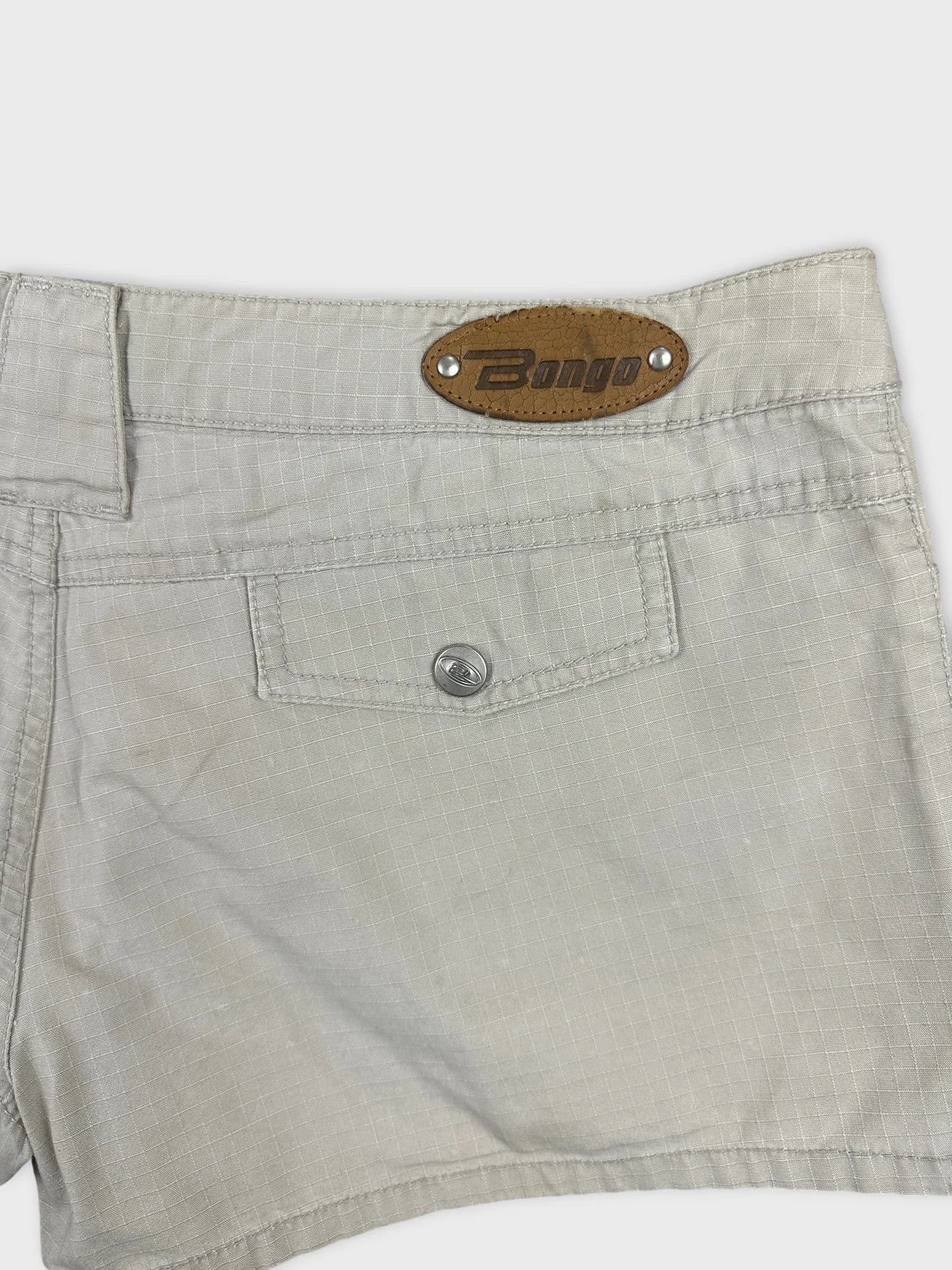 Detail view of light gray jean shorts featuring a leather logo patch.