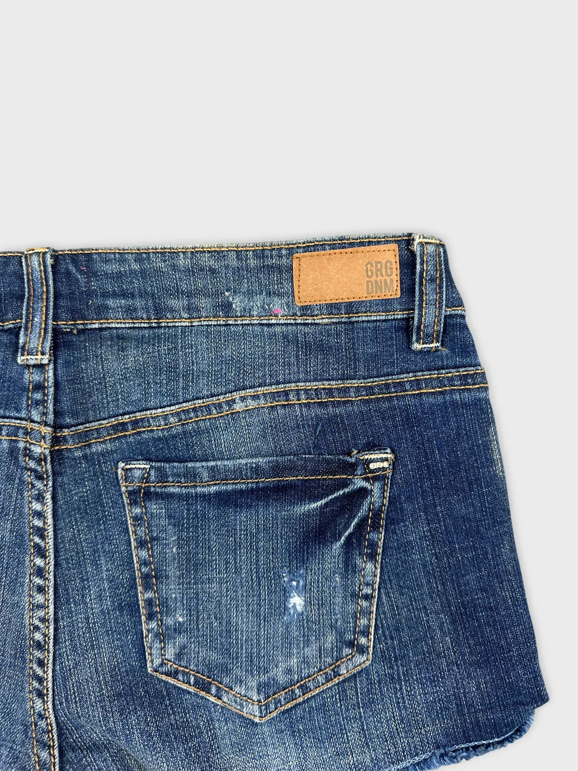 Detail view of blue jean shorts featuring a back pocket and waistband.