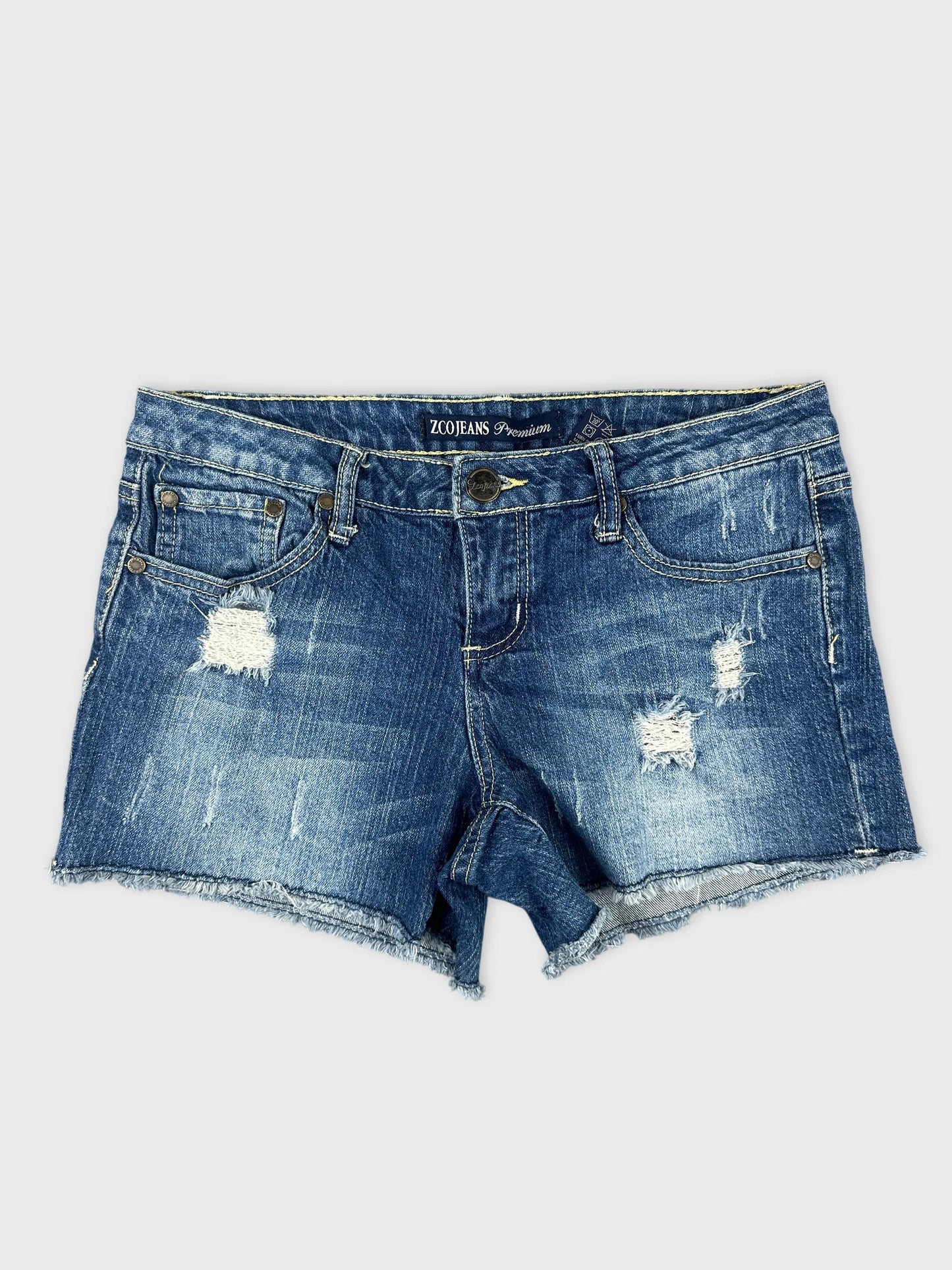 Front view of distressed denim shorts in blue with frayed hem.