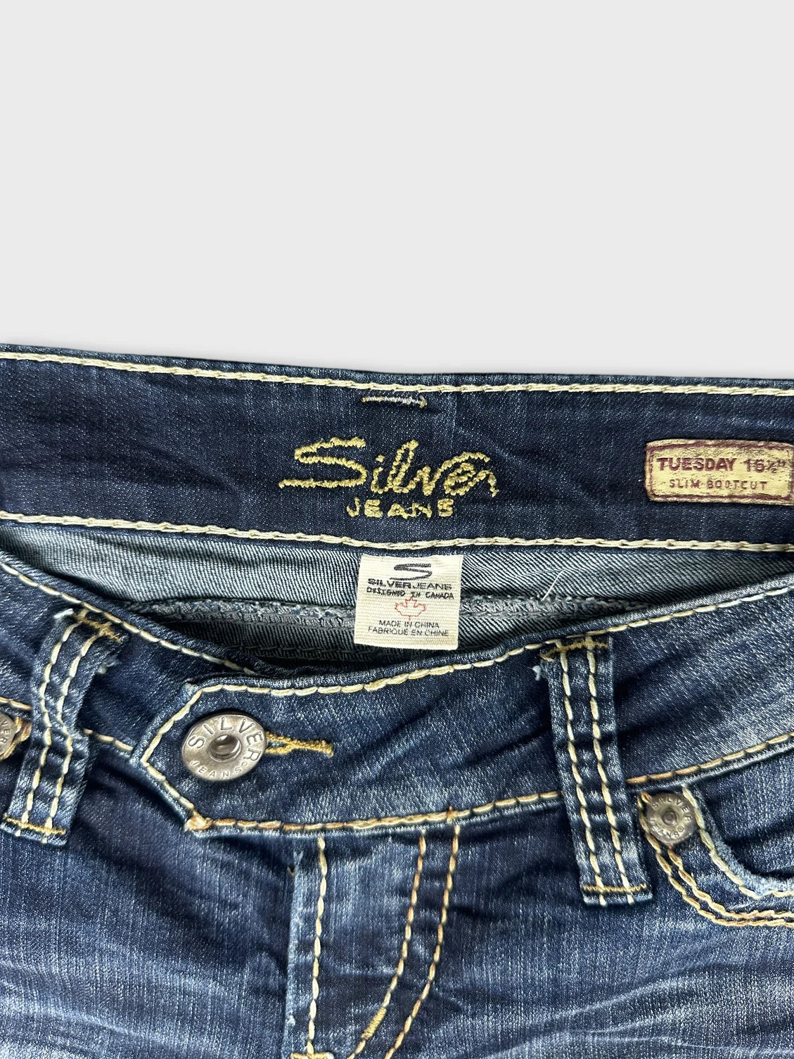 Back view of dark blue jeans featuring yellow stitching and button detail.
