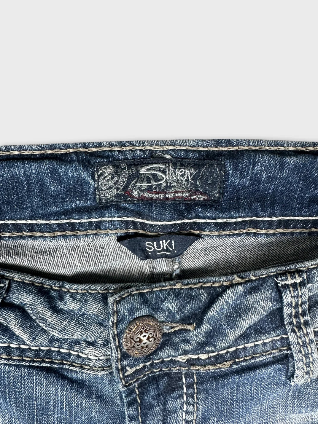Detail view of blue jeans featuring a decorative button and tag inside.