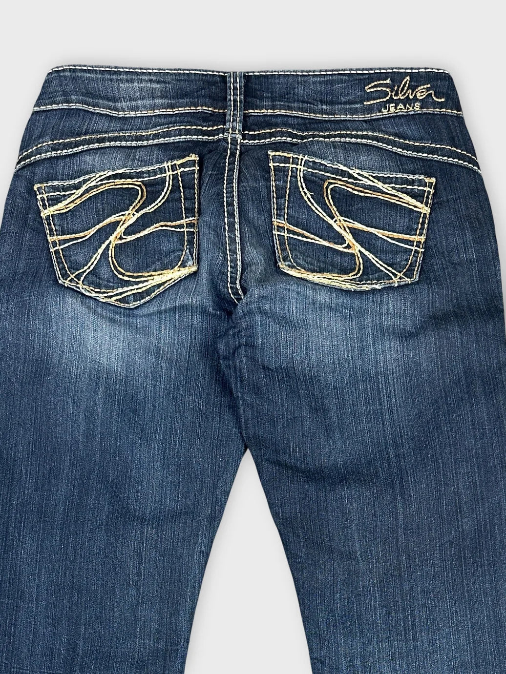 Detail view of dark denim jeans featuring embroidered back pockets