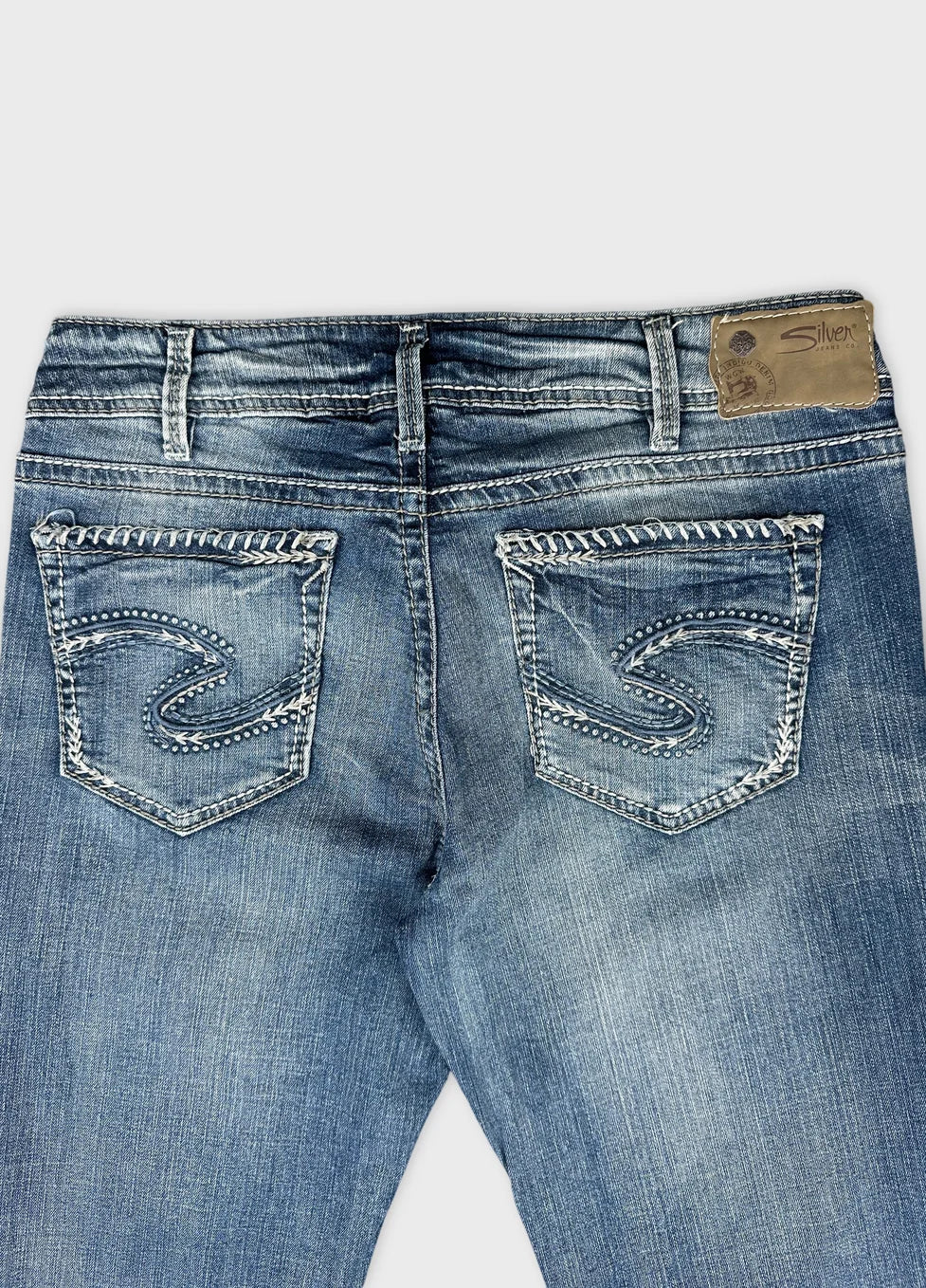Detail view of blue denim jeans featuring embroidered back pockets.