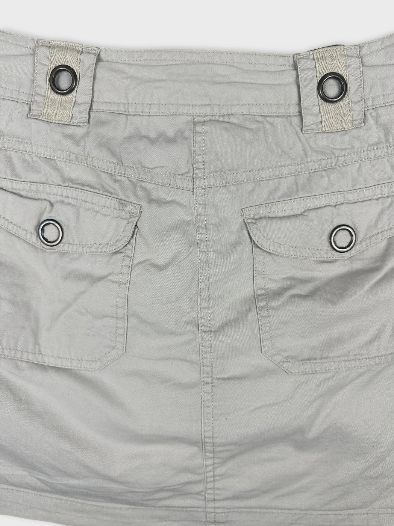Detail view of a mini skirt in light gray with button closures and pockets.