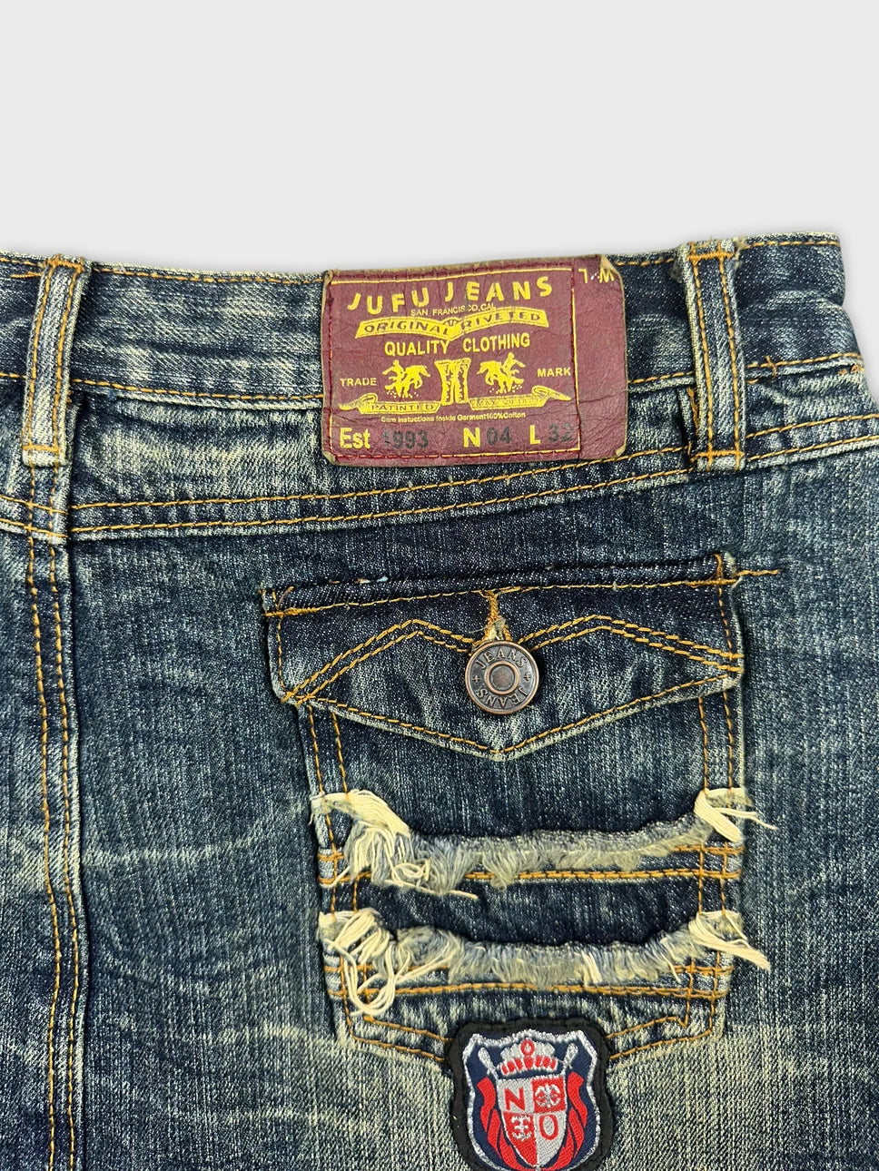 Detail view of a vintage denim mini skirt with distressed patches and a blue color.