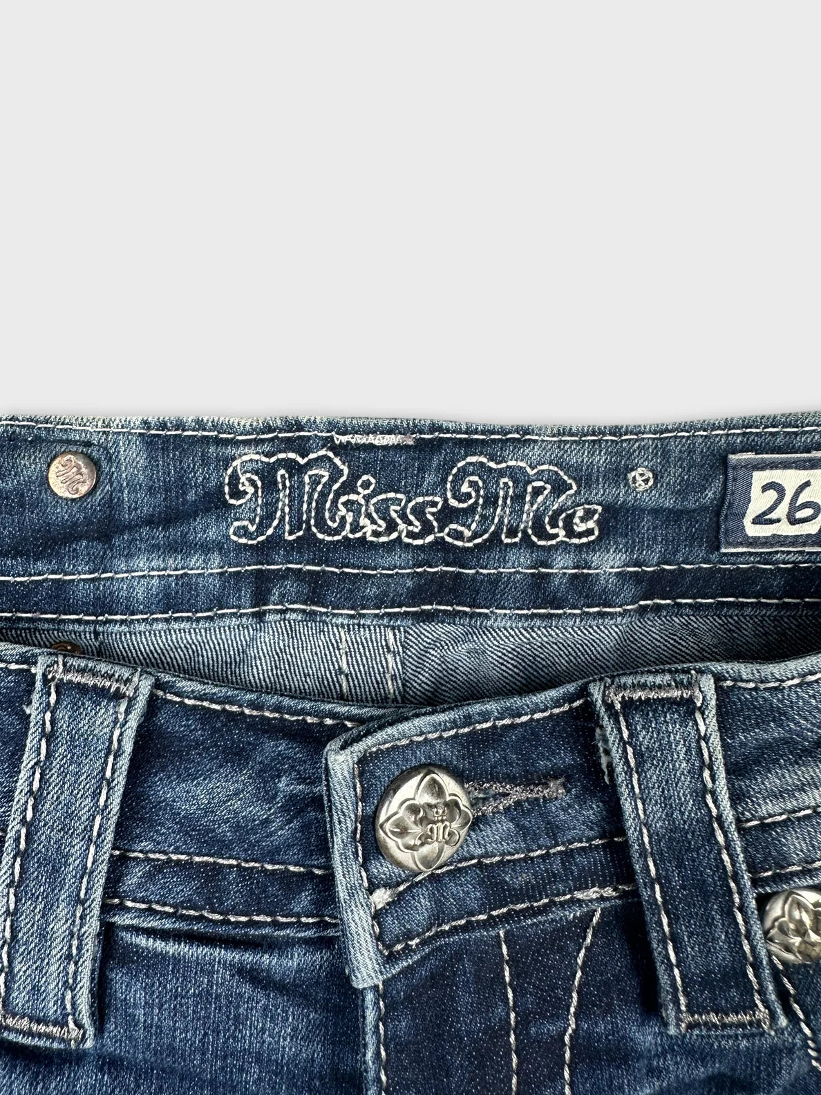 Detail view of blue denim shorts featuring embroidered brand logo and decorative stitching.