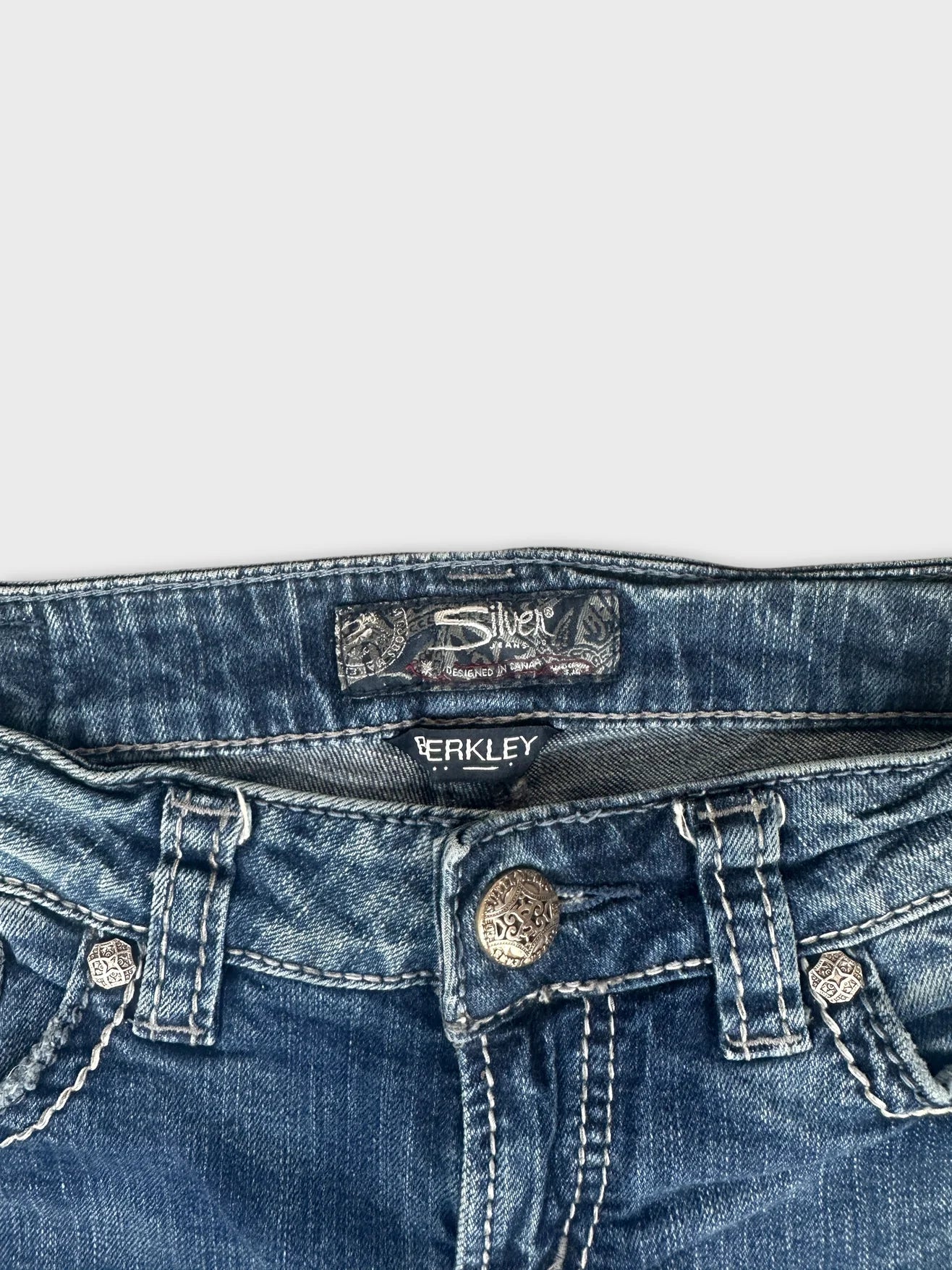 Detail view of women's denim jeans in dark blue with metal button embellishment.