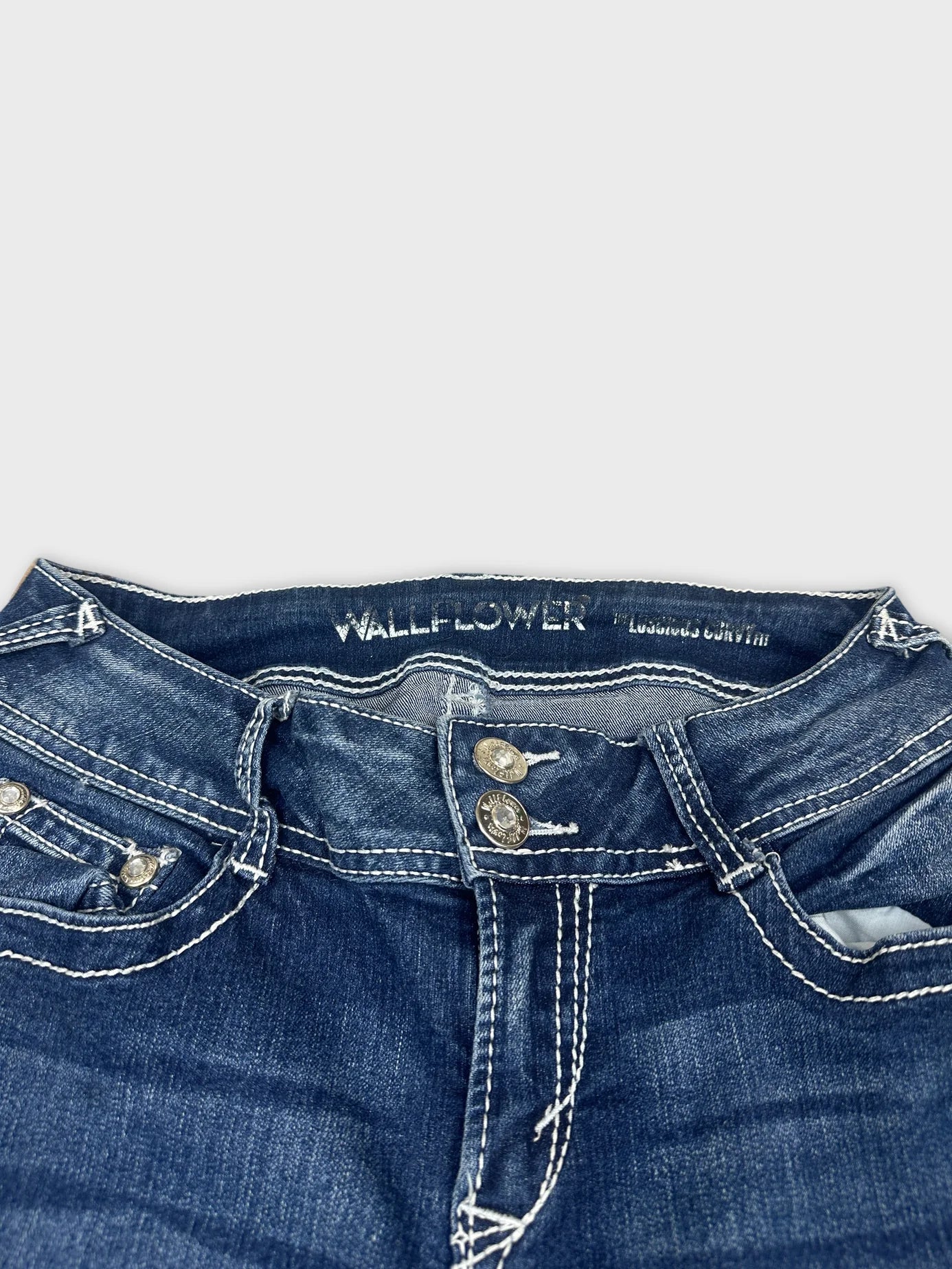 Detail view of women's denim jeans in dark blue with silver buttons.