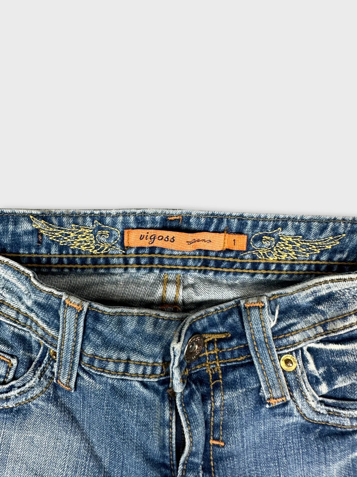 Detail view of women denim jeans in light blue with embroidered wings on waistband.