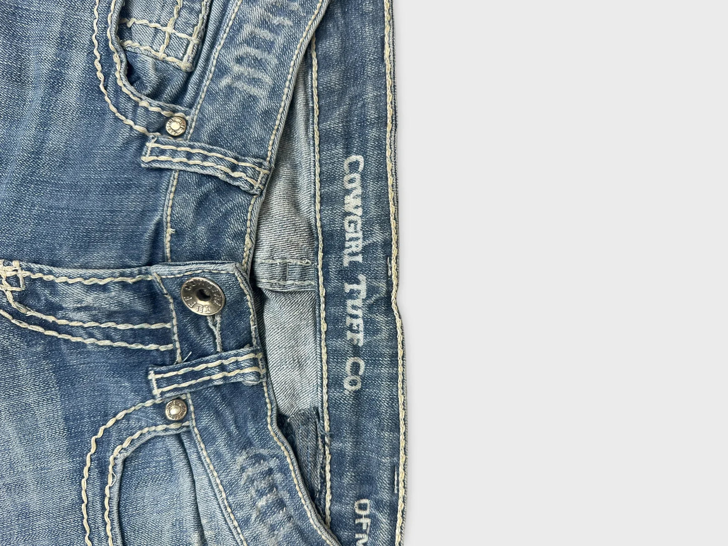 Detail view of blue denim jeans featuring decorative stitching and metal button.